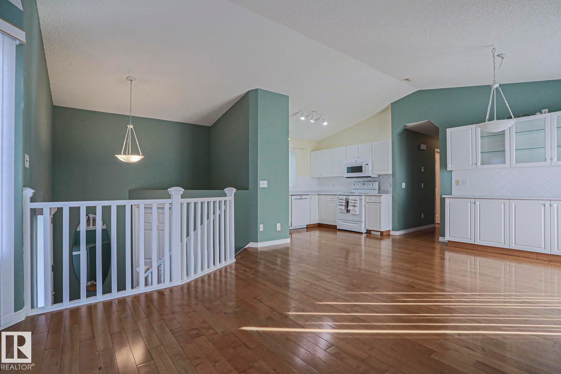 Wood-finish flooring, white kitchen cabinetry with glass panel inserts, white appliances, and a white balustrade - 15031 135 Street Nw, Edmonton, AB