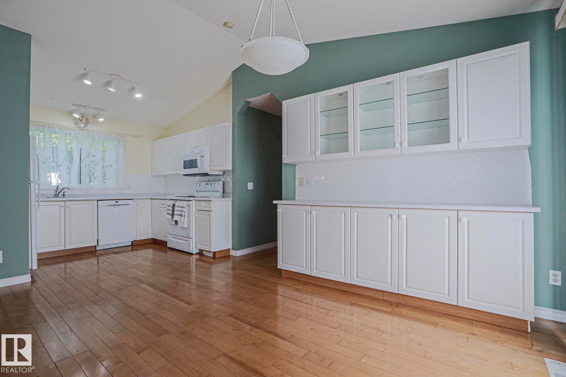 Hardwood-finish flooring, vaulted ceiling, white cabinetry with glass-front uppers, white appliances, and a tiled backsplash - 15031 135 Street Nw, Edmonton, AB