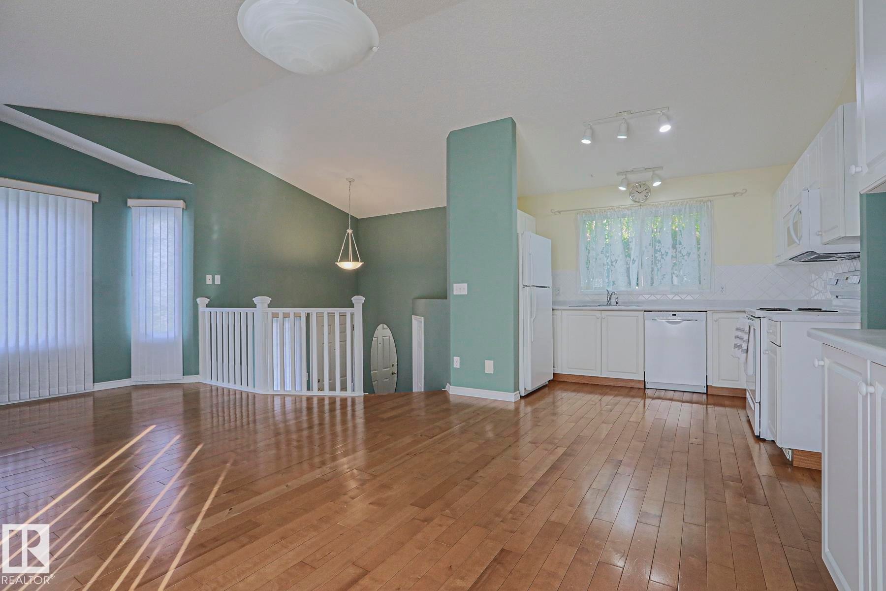 Open-concept living area with vaulted ceilings, wood-finish flooring, and a kitchen featuring white cabinetry and appliances - 15031 135 Street Nw, Edmonton, AB
