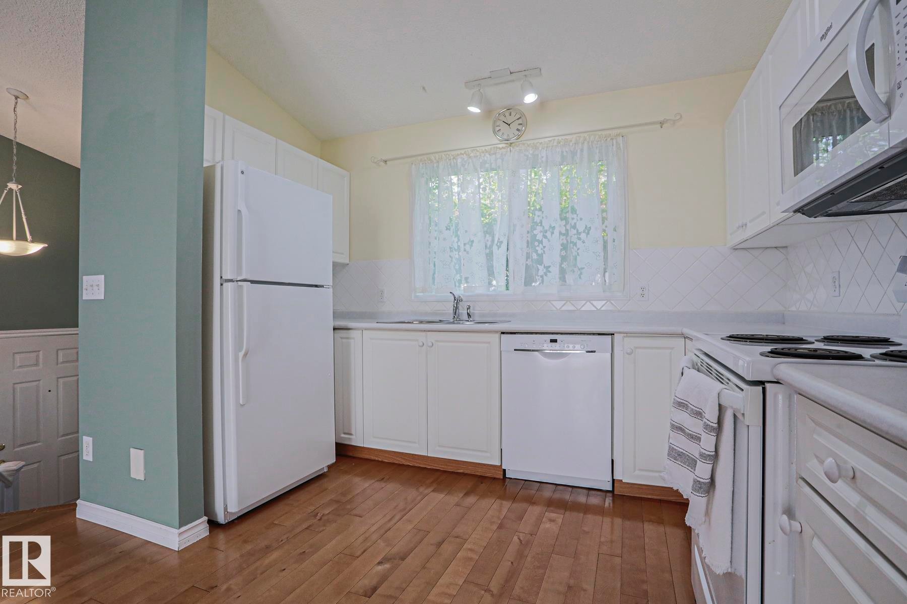 Kitchen featuring wood-finish flooring, white cabinetry, a white tile backsplash, and track lighting - 15031 135 Street Nw, Edmonton, AB