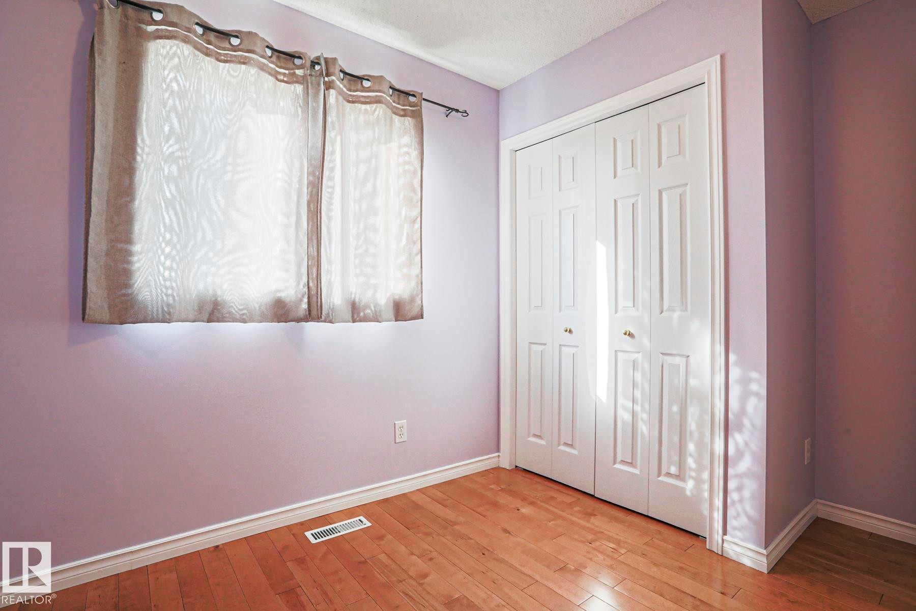 Wood-finish flooring with white trim, featuring a bifold closet door with gold-tone hardware - 15031 135 Street Nw, Edmonton, AB