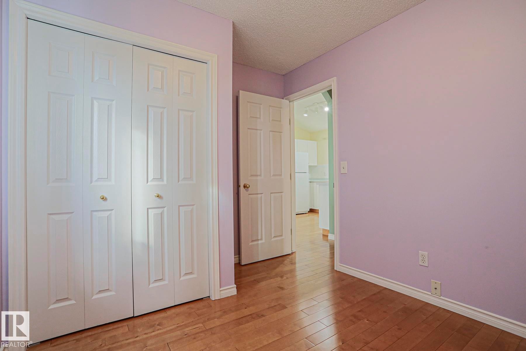 Wood-finish flooring throughout, bright lavender wall finish, and white bi-fold closet doors with brass hardware - 15031 135 Street Nw, Edmonton, AB