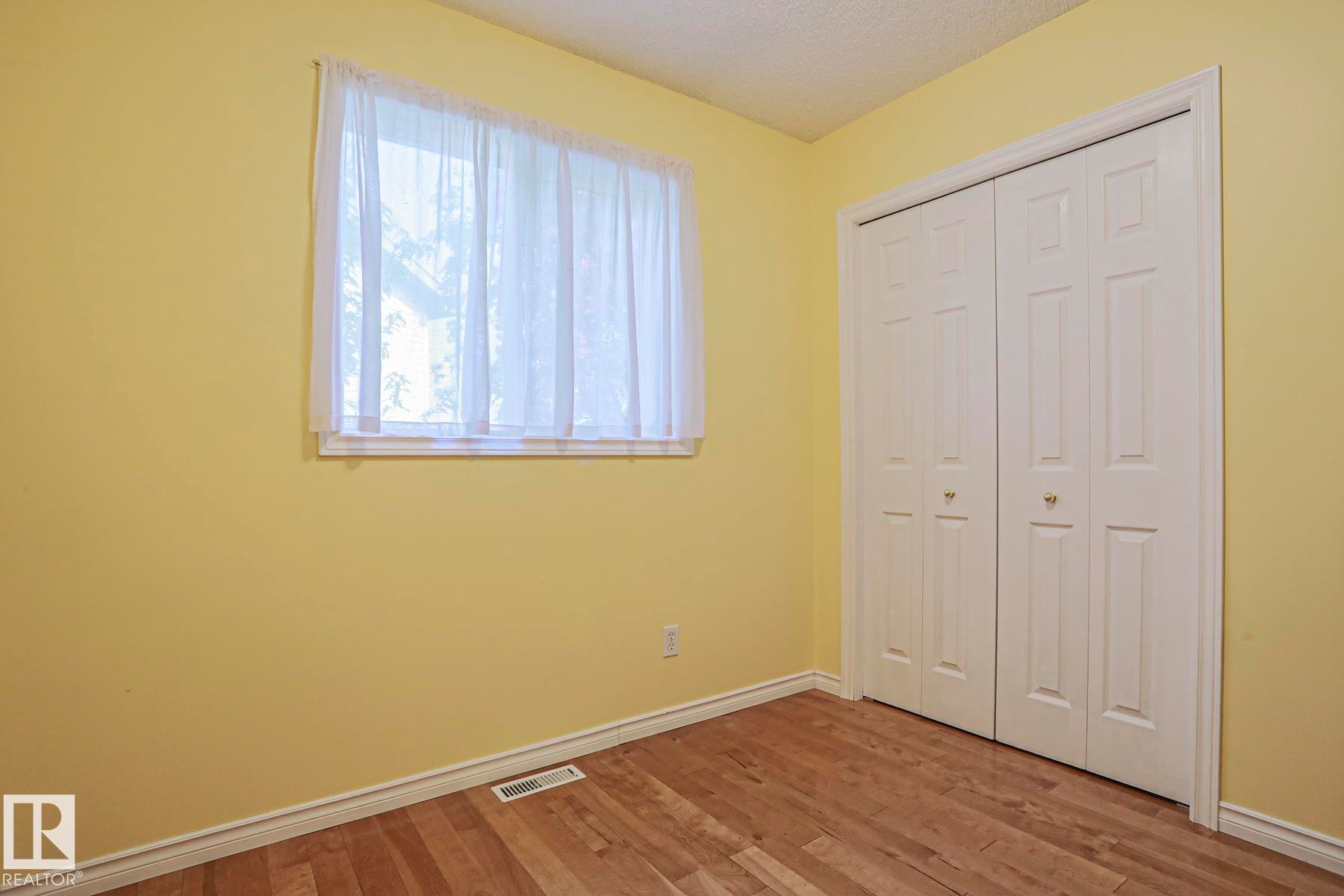 Wood-finish flooring with white trim, a window, and a built-in bifold closet - 15031 135 Street Nw, Edmonton, AB