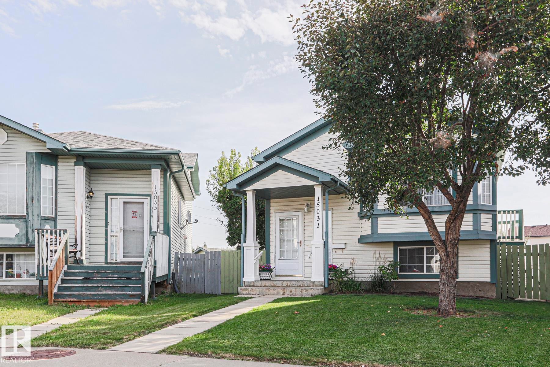 Bi Level property featuring light-colored siding with dark trim, a covered front entryway, and an established front yard tree - 15031 135 Street Nw, Edmonton, AB