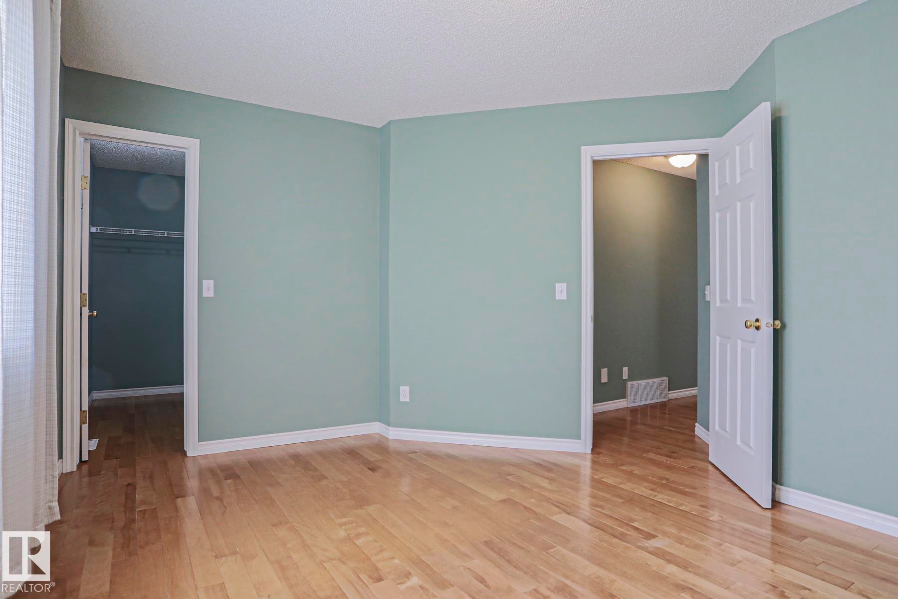 Wood-finish flooring with light-toned walls, white trim, and a paneled door - 15031 135 Street Nw, Edmonton, AB