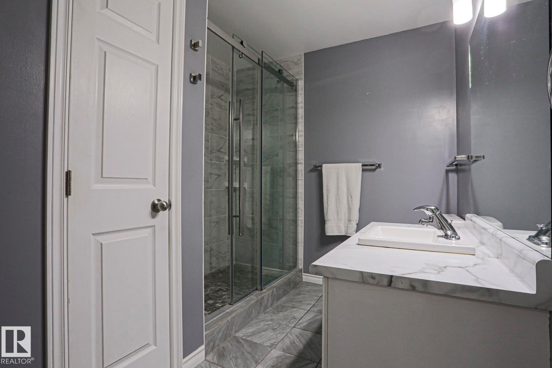 Vanity with integrated sink and chrome faucet, glass-enclosed shower with tile surround, and tile flooring - 15031 135 Street Nw, Edmonton, AB