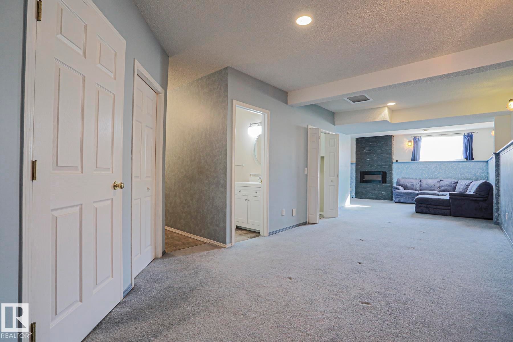 Recessed lighting, light gray carpeting, built-in fireplace with dark stone surround, white paneled doors, and a bathroom with white vanity - 15031 135 Street Nw, Edmonton, AB