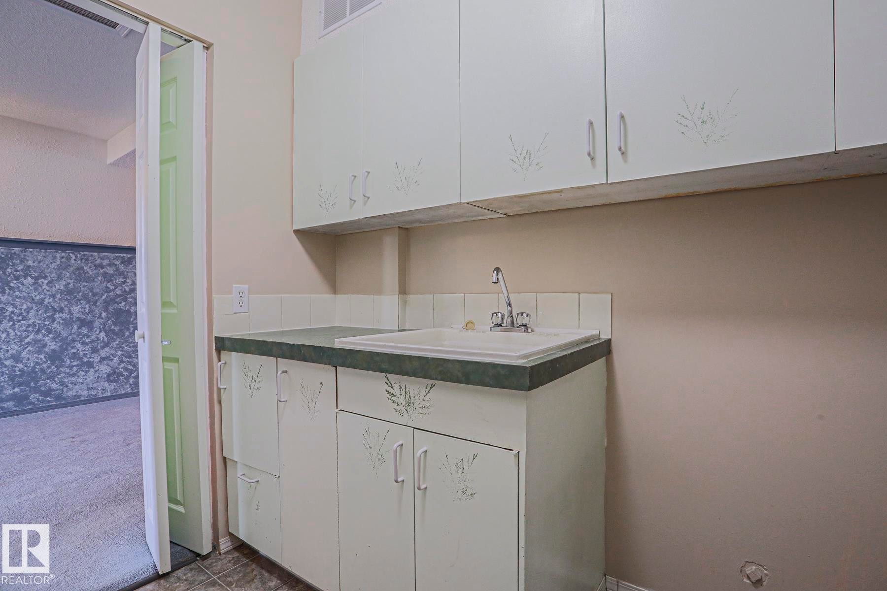 Built-in upper and lower cabinetry, integrated sink with faucet, tile backsplash, and dark countertop surface - 15031 135 Street Nw, Edmonton, AB