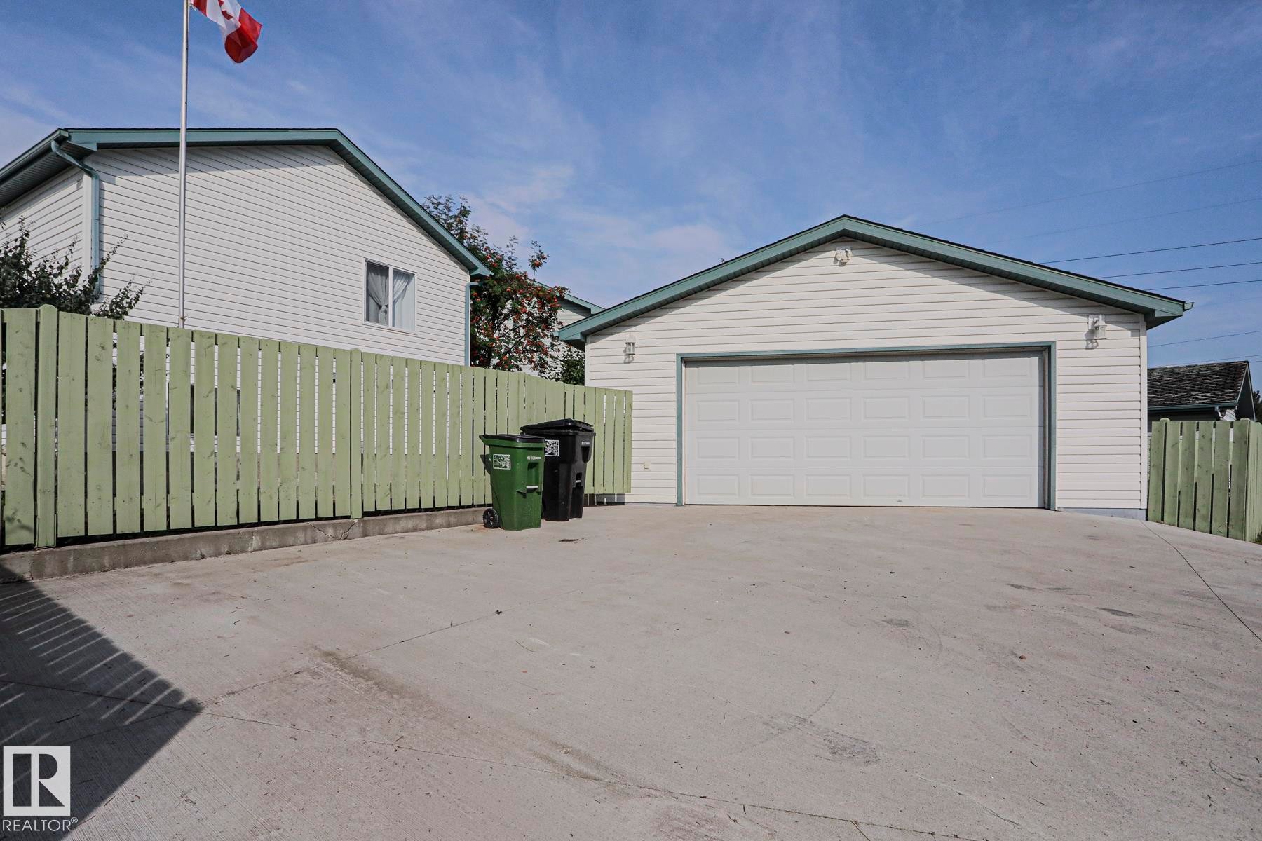 Detached two-car garage with white paneled door, concrete driveway, and light green privacy fencing - 15031 135 Street Nw, Edmonton, AB