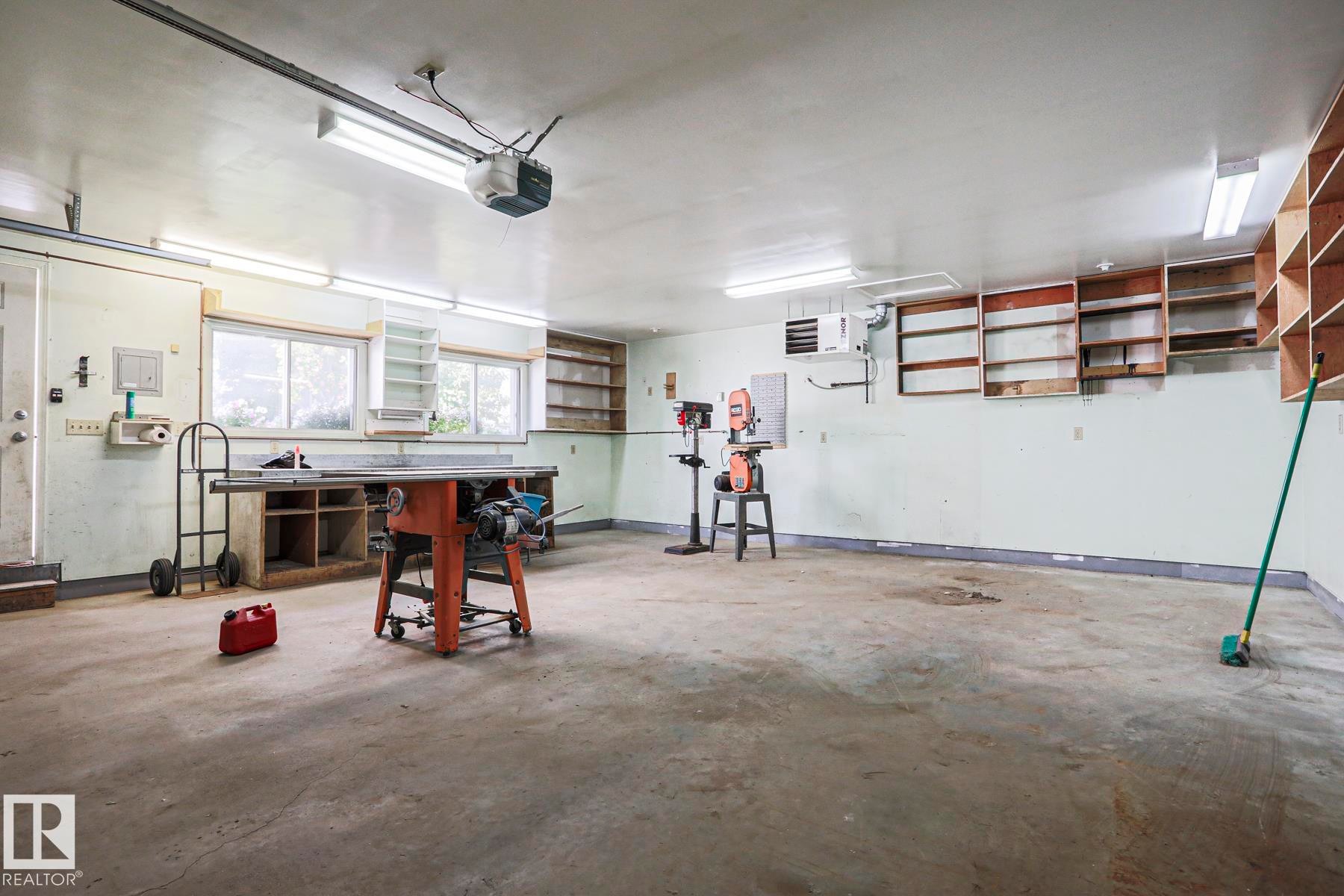 Spacious garage with concrete flooring, multiple windows for natural light, fluorescent overhead lighting, and built-in wall shelving - 15031 135 Street Nw, Edmonton, AB