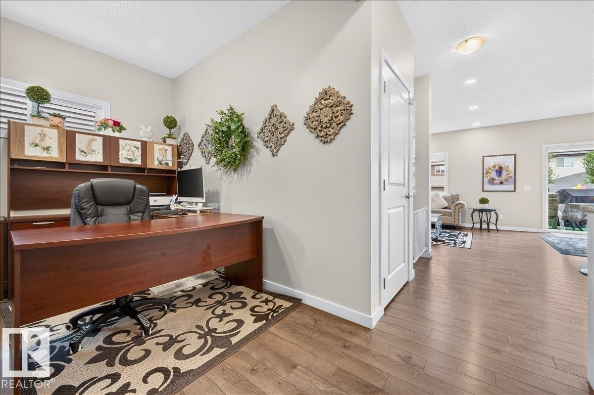 Dedicated office space featuring a built-in desk with overhead storage, wood-finish flooring, white trim, and a window with horizontal blinds - 2709 Collins Crescent Sw, Edmonton, AB - Indoor Photo Showing Office