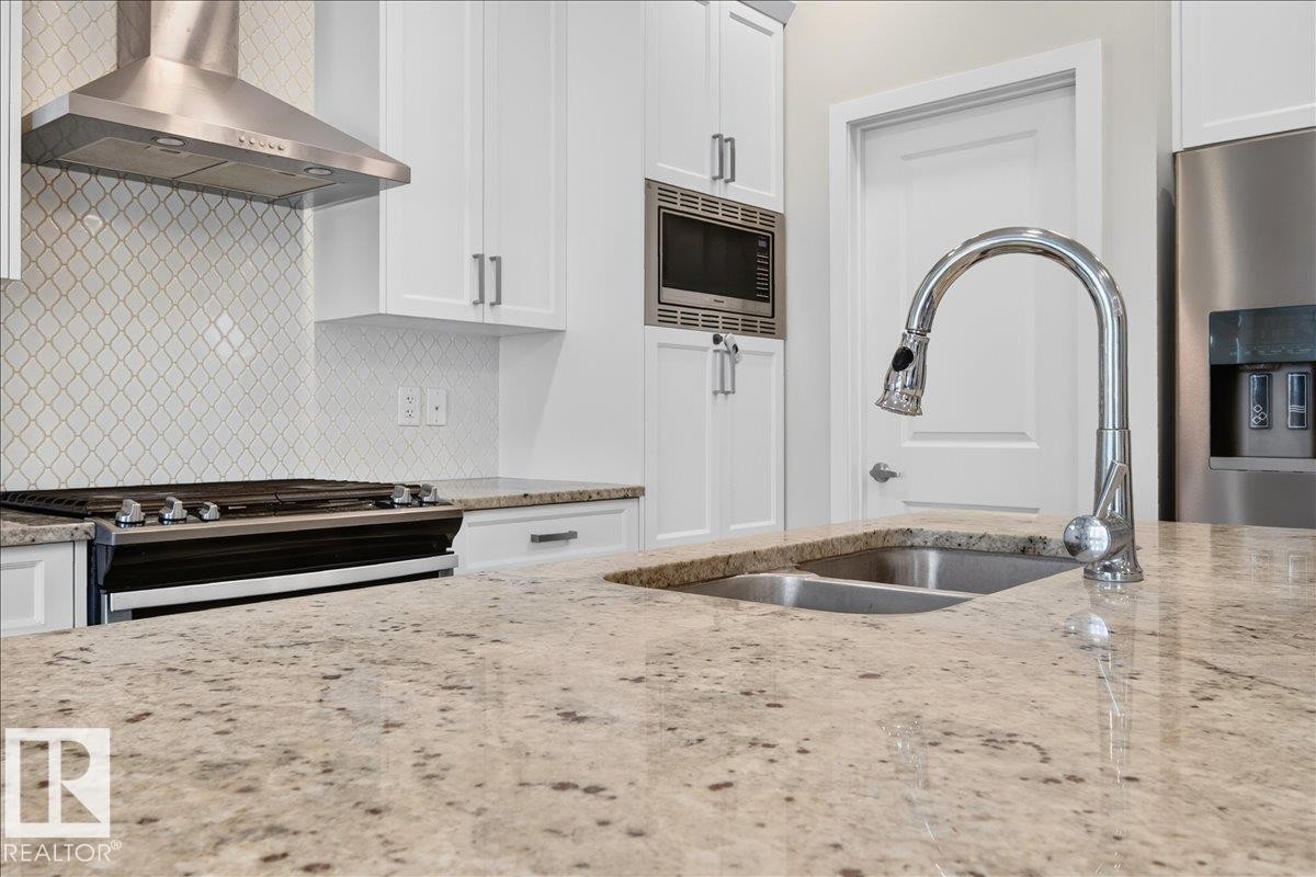 Kitchen featuring granite countertops, white cabinetry, a stainless steel range hood, a tiled backsplash, and a double basin sink with a chrome faucet - 2709 Collins Crescent Sw, Edmonton, AB - Indoor Photo Showing Kitchen With Stainless Steel Kitchen With Double Sink With Upgraded Kitchen