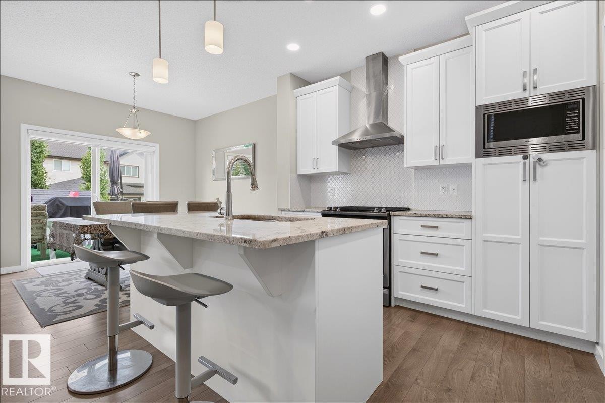 Modern kitchen featuring white cabinetry, granite countertops, a built-in microwave, stainless steel range hood, and wood-finish flooring - 2709 Collins Crescent Sw, Edmonton, AB - Indoor Photo Showing Kitchen With Upgraded Kitchen