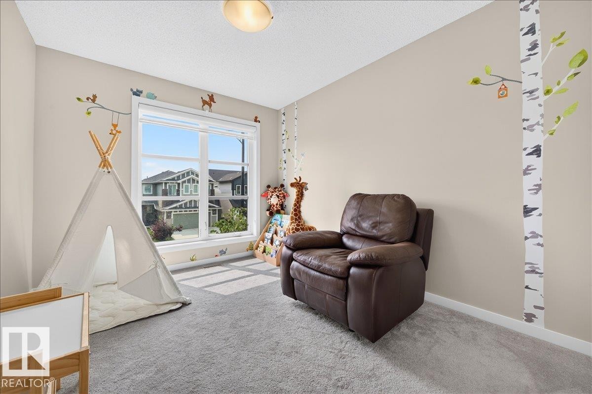Bright interior space with a large window, textured carpeting, neutral wall tones, and a semi-flush mount ceiling light fixture - 2709 Collins Crescent Sw, Edmonton, AB - Indoor