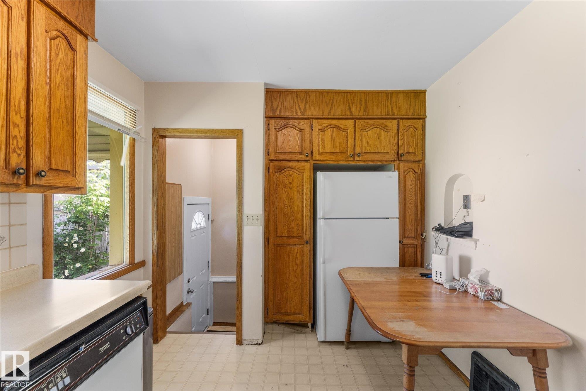 Wood cabinetry, light-toned countertop, tile backsplash, built-in dishwasher, and window with exterior landscaping - 9315 86 Street Nw, Edmonton, AB
