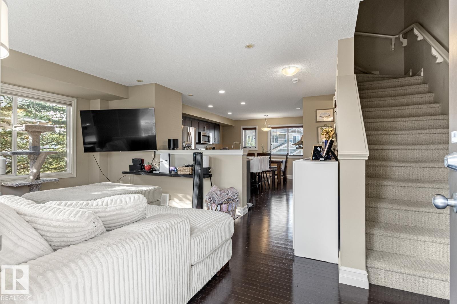 Hardwood-finish flooring, recessed lighting, large window, and carpeted staircase with wood handrail - 5319 3 Avenue Sw, Edmonton, AB