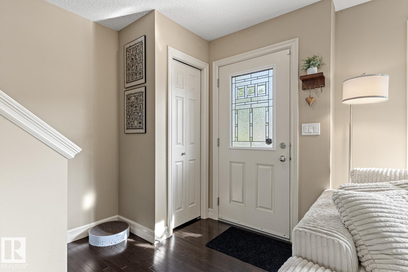Entryway featuring dark wood-finish flooring, a white paneled door with decorative glass, and a closet with bifold doors - 5319 3 Avenue Sw, Edmonton, AB
