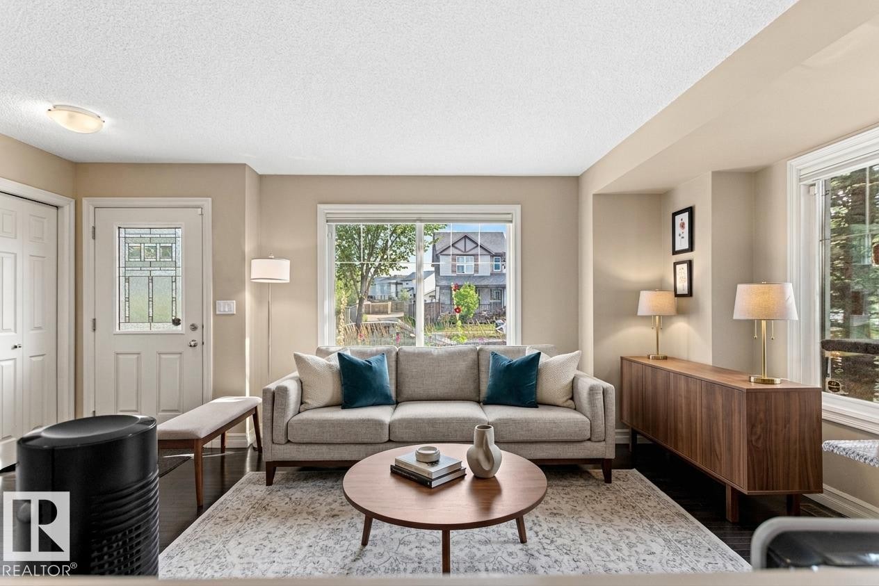 Living area with dark wood-finish flooring, light neutral wall paint, and multiple windows - 5319 3 Avenue Sw, Edmonton, AB