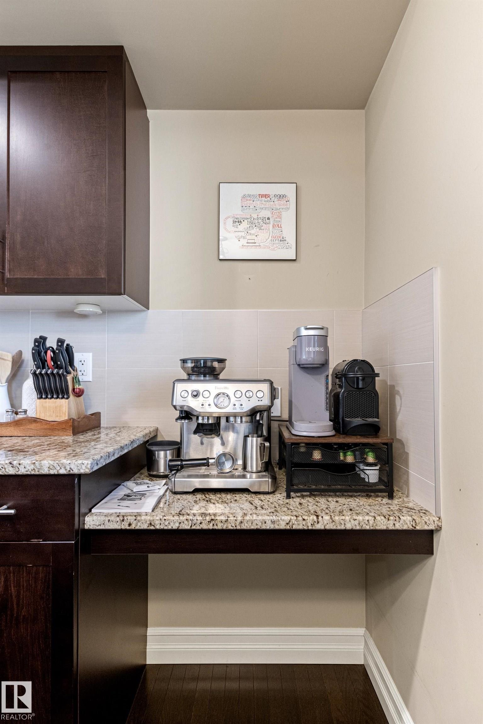 Granite-finish countertop, dark wood-finish cabinetry, tile backsplash, built-in desk or workstation, and wood-finish flooring - 5319 3 Avenue Sw, Edmonton, AB