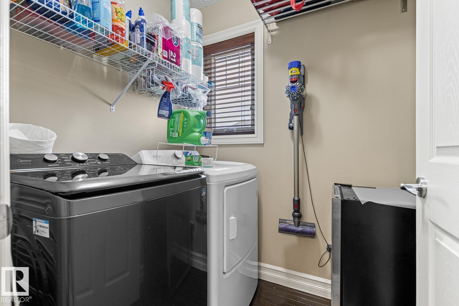 Laundry area featuring a window with blinds, wall-mounted shelving, and wood-finish flooring - 5319 3 Avenue Sw, Edmonton, AB
