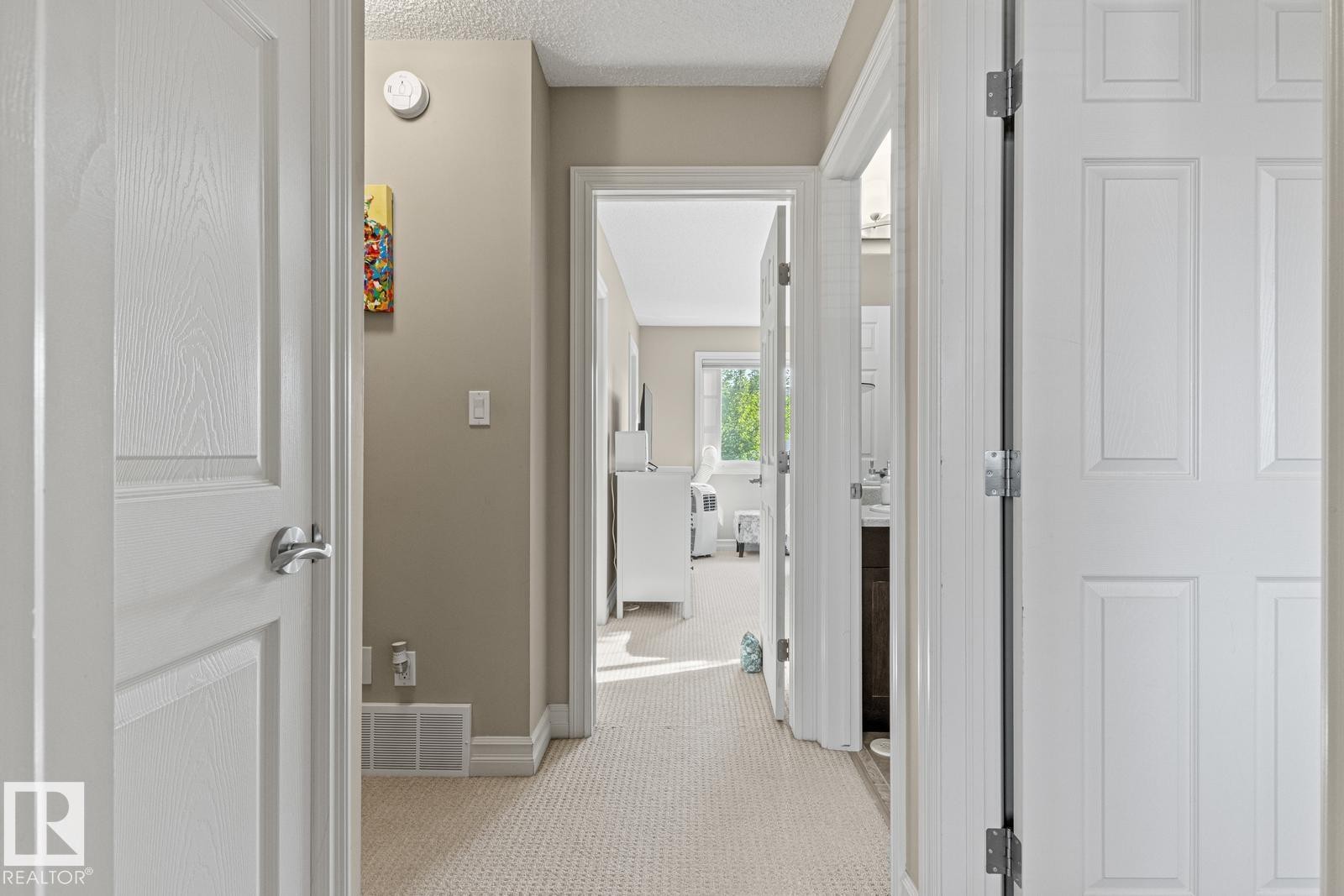 Hallway featuring light neutral-toned walls, textured carpeting, white baseboards, and white paneled doors with chrome hardware - 5319 3 Avenue Sw, Edmonton, AB