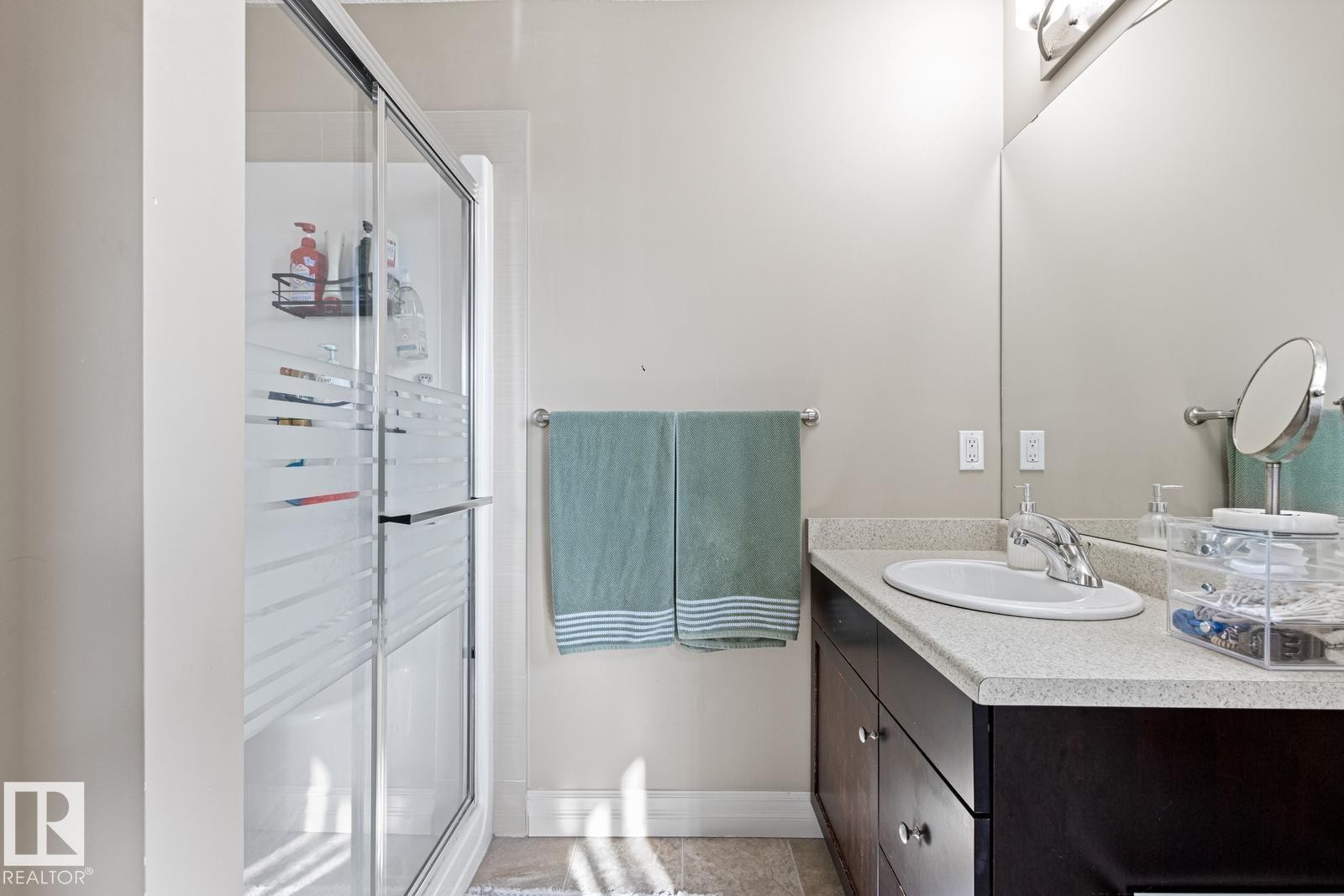 Shower with sliding frosted glass doors, a vanity with an integrated sink, a chrome faucet, and a large wall-mounted mirror - 5319 3 Avenue Sw, Edmonton, AB