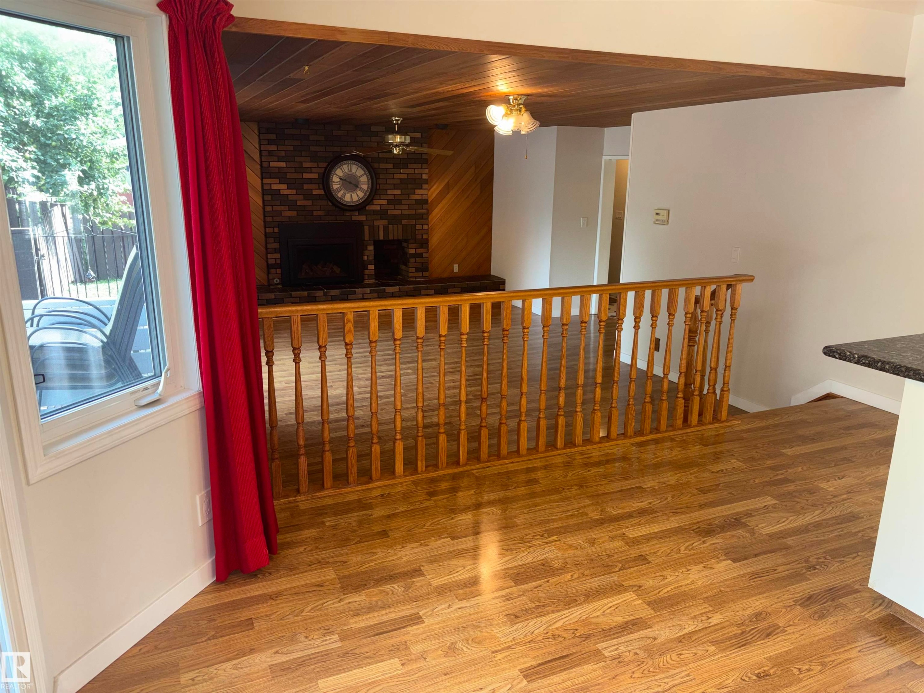 Wood-finish flooring throughout, with a recessed fireplace and brick surround, and wood paneling on walls and ceiling - 4027 74 Street Nw, Edmonton, AB
