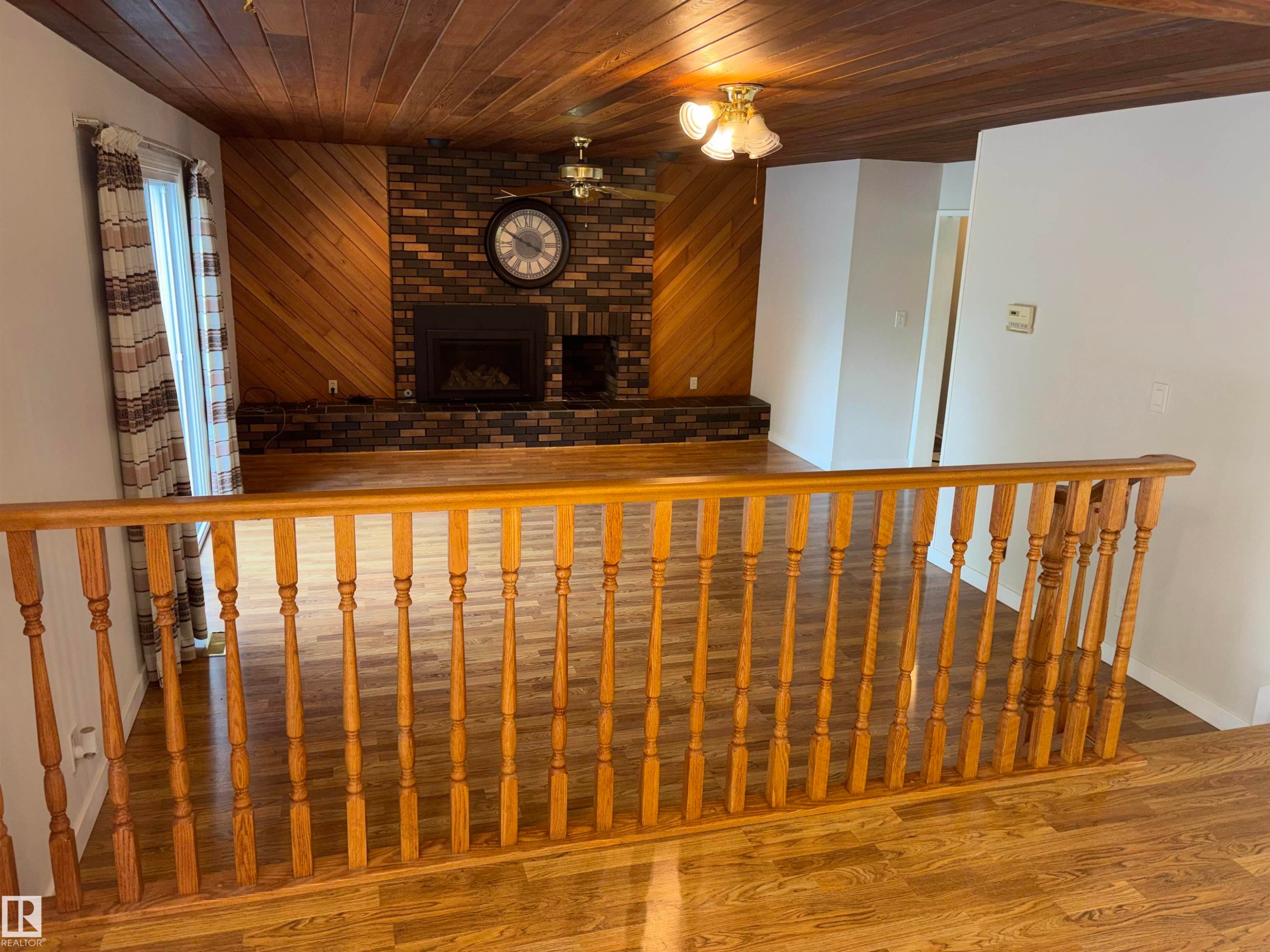 Wood-finish flooring throughout, wood-paneled ceiling, brick fireplace with mantel, wood-paneled accent wall, and decorative wood railing - 4027 74 Street Nw, Edmonton, AB