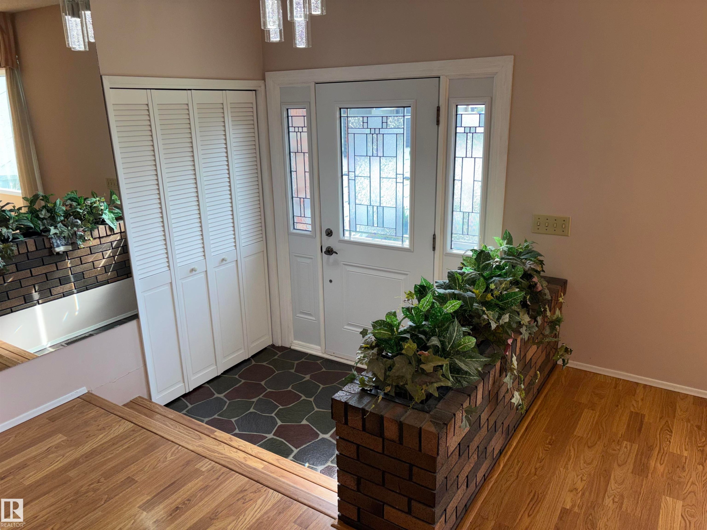 Front entry featuring a decorative glass paneled door, sidelights, bi-fold louvered closet doors, and multi-tone irregular tile flooring - 4027 74 Street Nw, Edmonton, AB
