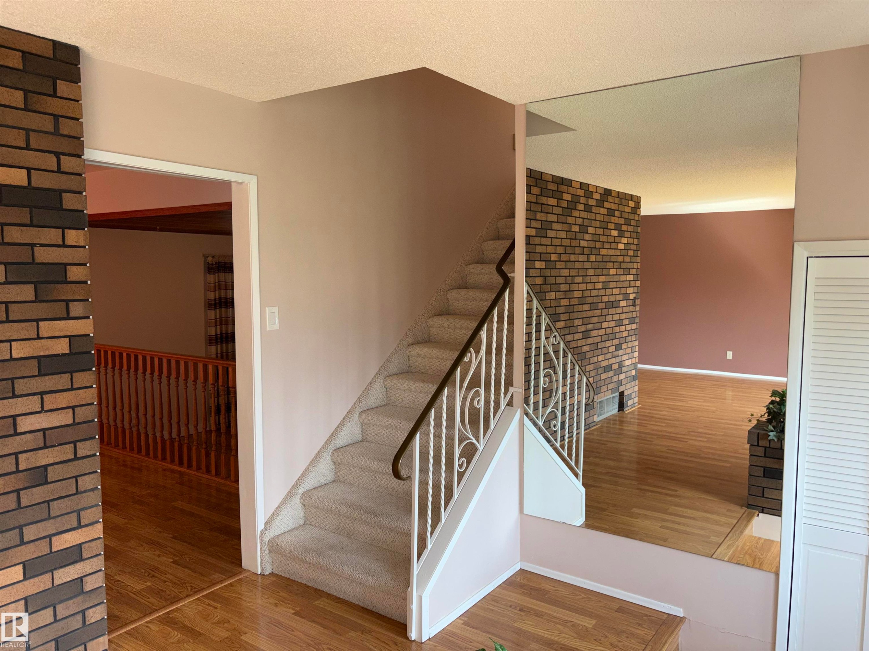 Carpeted staircase with an ornamental wrought iron railing, brick accent wall, and wood-finish flooring - 4027 74 Street Nw, Edmonton, AB