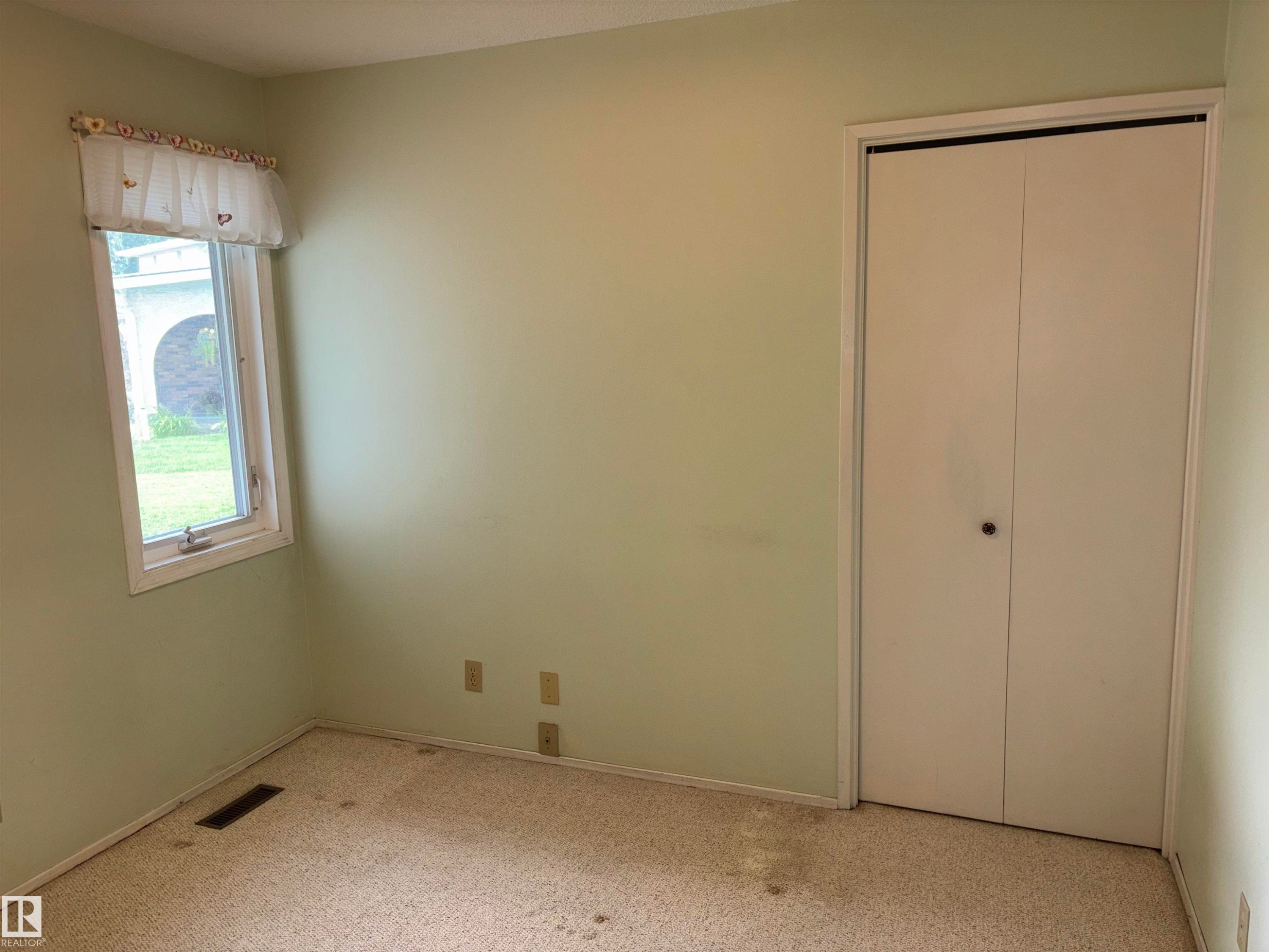 Window with exterior landscaping visible, light-colored walls, and a bi-fold closet door - 4027 74 Street Nw, Edmonton, AB