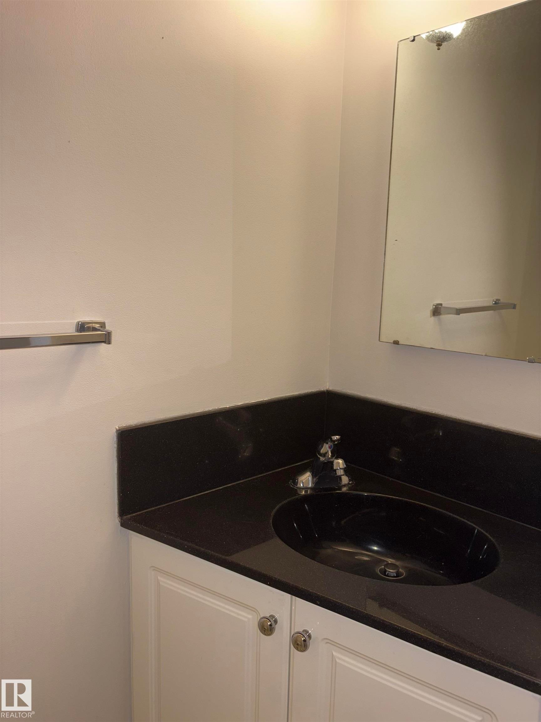 White vanity cabinetry with polished chrome hardware, dark stone countertop, integrated black oval sink, and wall-mounted mirror - 4027 74 Street Nw, Edmonton, AB