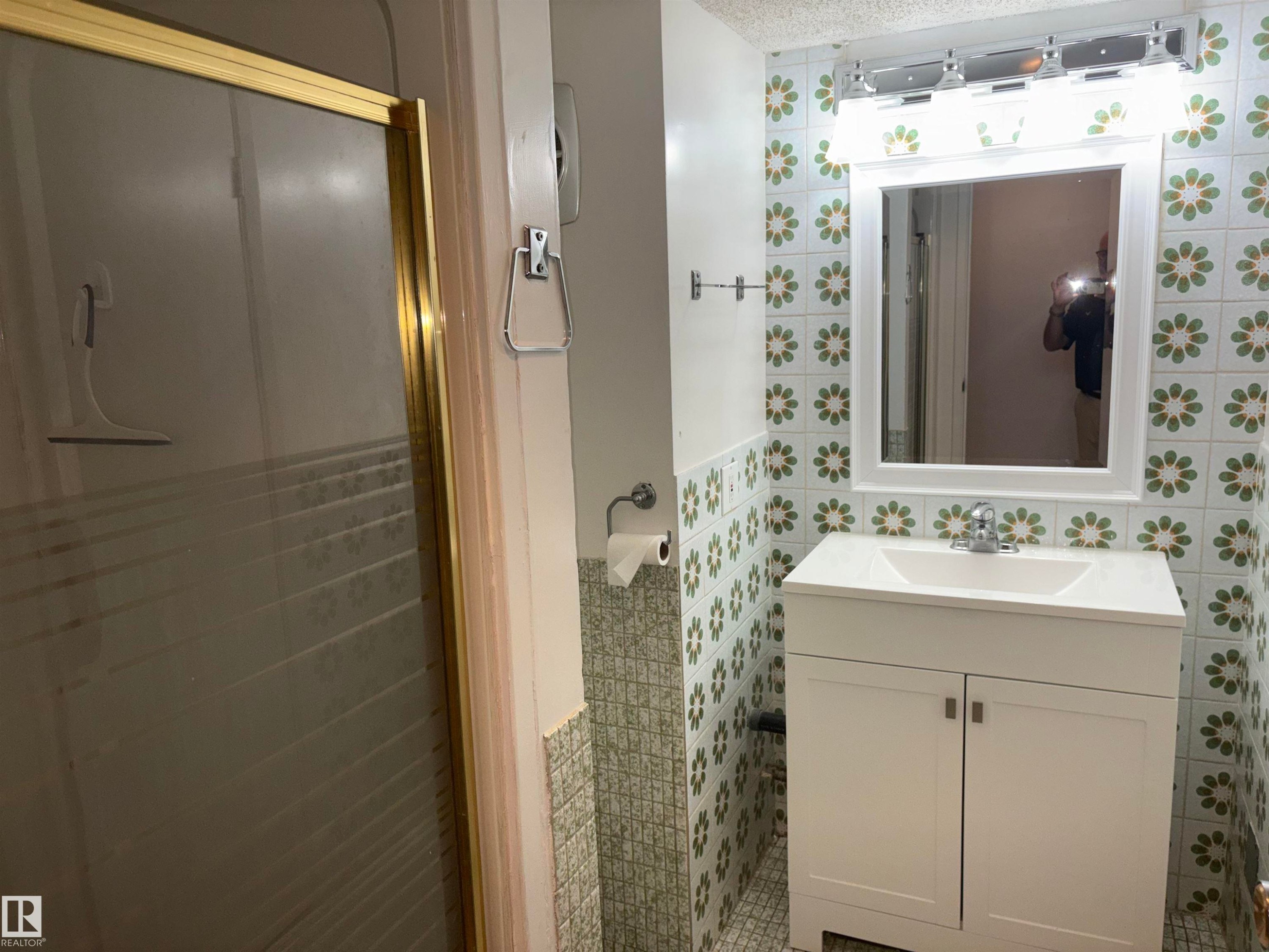 Vanity with white cabinetry and integrated sink, chrome faucet, wall-mounted mirror, and decorative tiled walls - 4027 74 Street Nw, Edmonton, AB