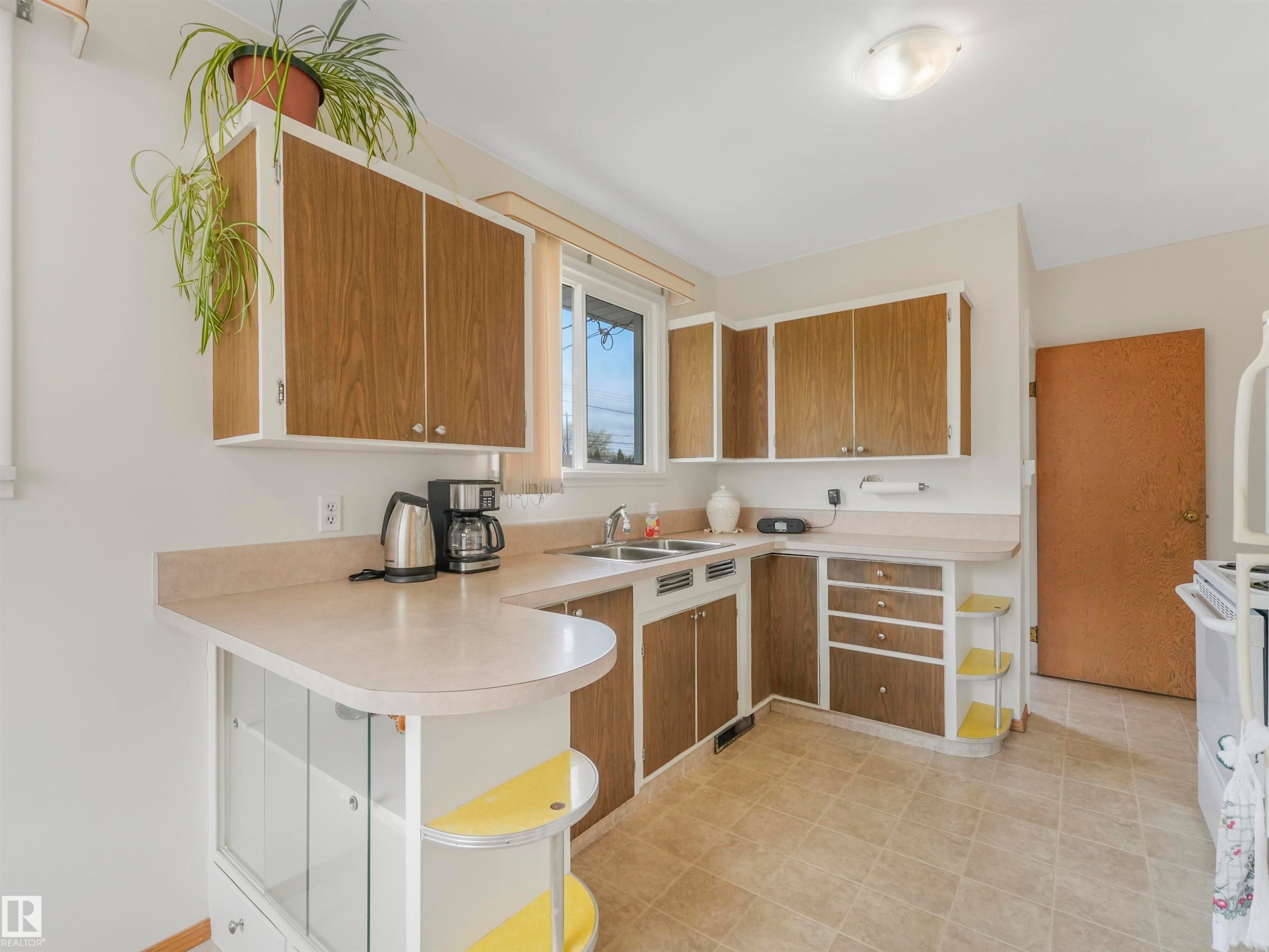 Kitchen featuring wood-finish cabinetry, a double basin sink, and a breakfast bar with built-in shelving - 12614 69 Street Nw, Edmonton, AB