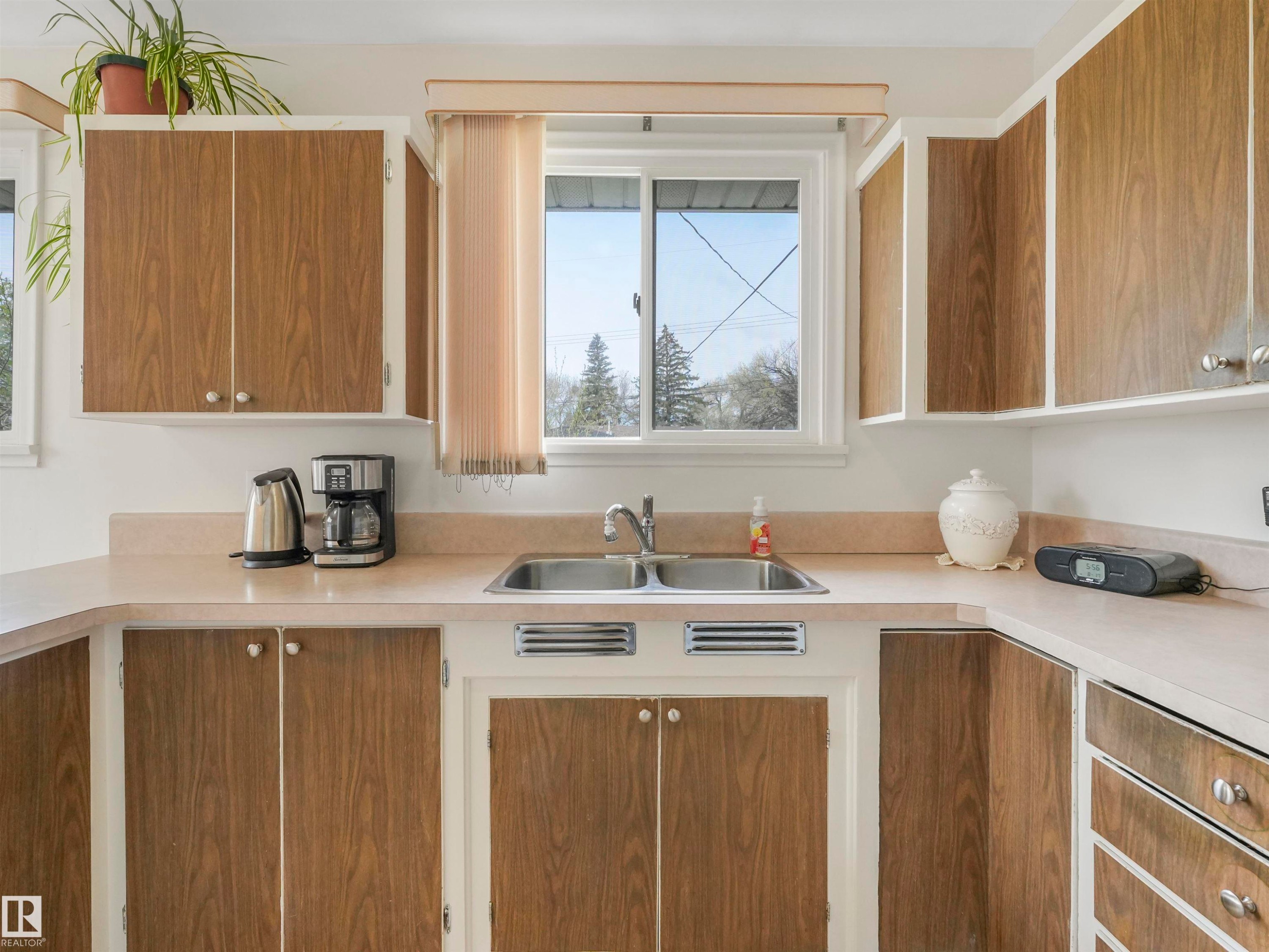 Wood-finish upper and lower cabinetry with integrated hardware, dual stainless steel sink, and light-toned countertops - 12614 69 Street Nw, Edmonton, AB