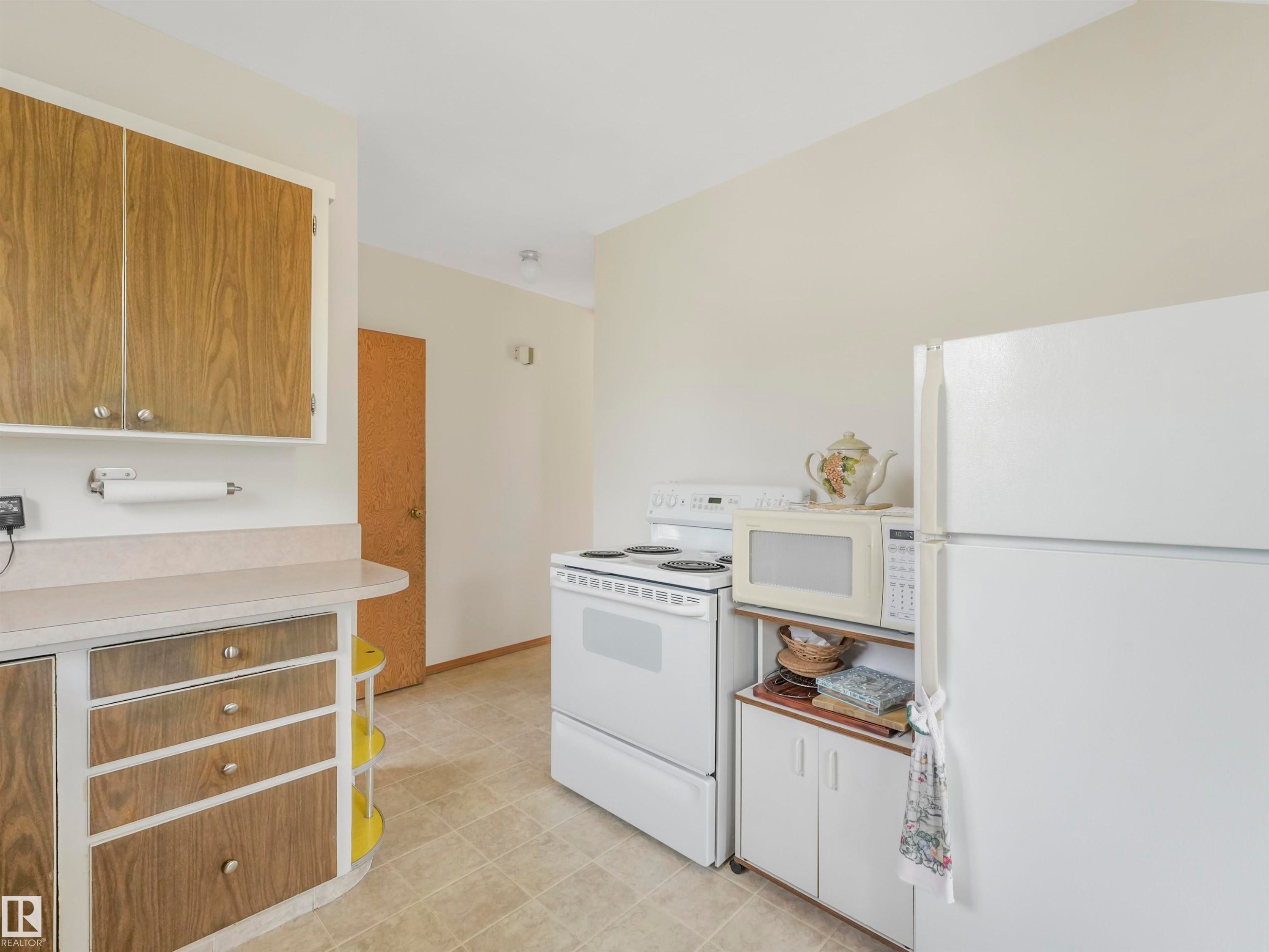 Kitchen featuring wood-finish cabinetry, light-toned countertops, and a white appliance suite - 12614 69 Street Nw, Edmonton, AB