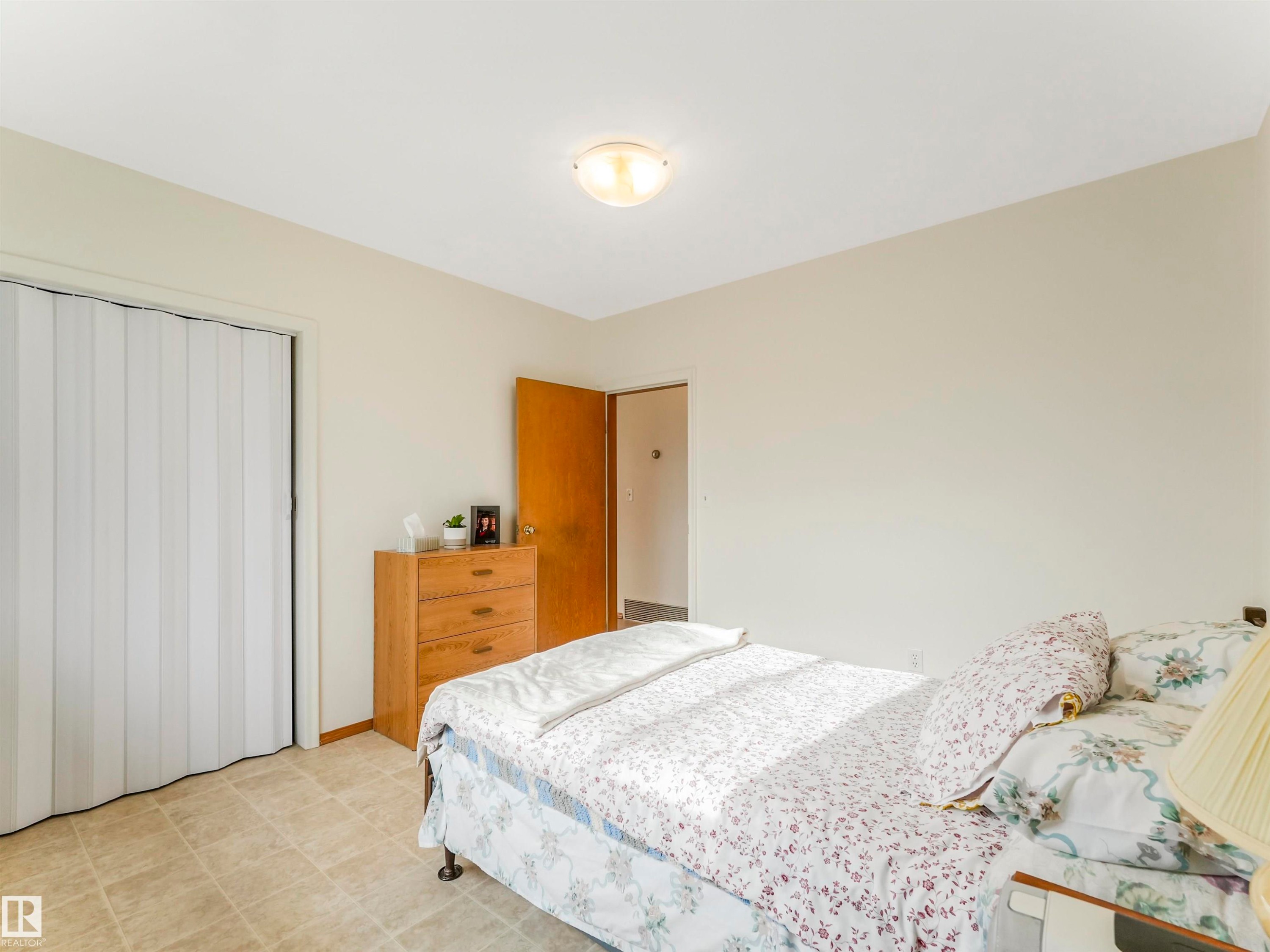 Textured accordion closet door, neutral wall tones, semi-flush ceiling light fixture, wood-finish interior door, tiled flooring - 12614 69 Street Nw, Edmonton, AB