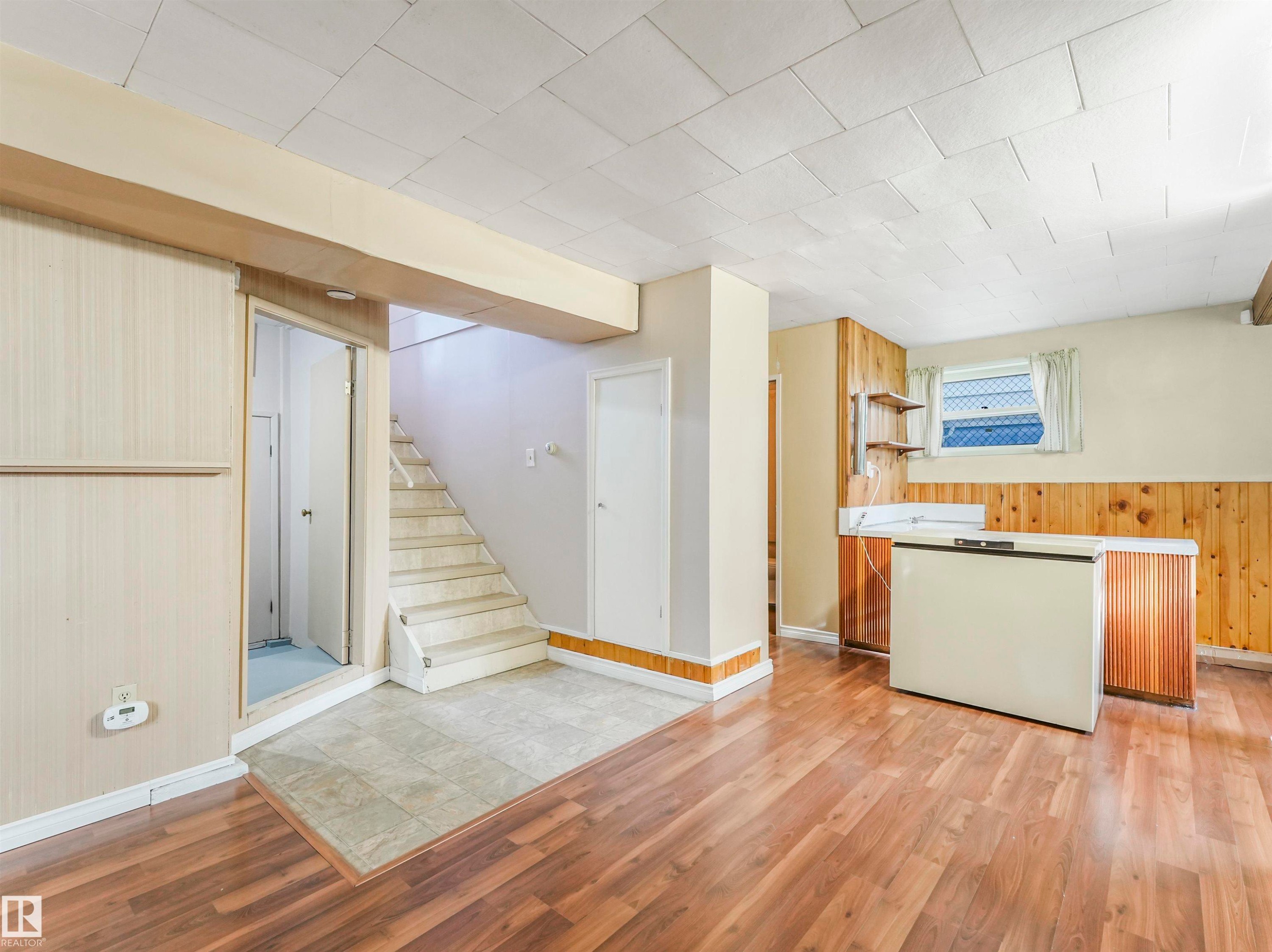 Wood-finish flooring, staircase with carpeted treads, paneled walls, built-in shelving, and a window with blinds - 12614 69 Street Nw, Edmonton, AB