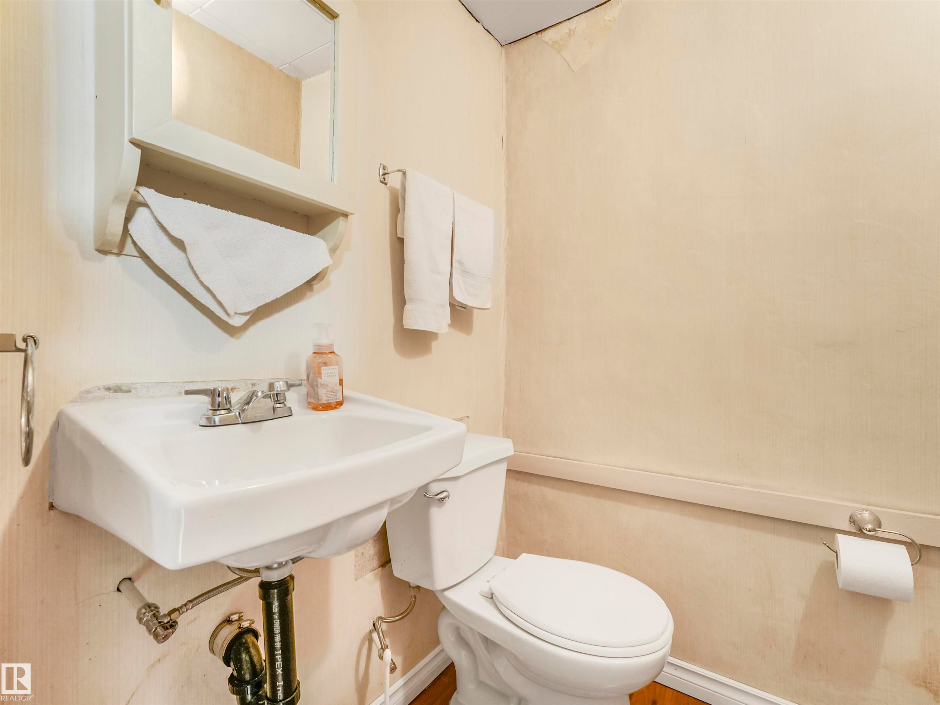 Pedestal sink with chrome faucet, wall-mounted mirror, white toilet, and wood-finish flooring - 12614 69 Street Nw, Edmonton, AB