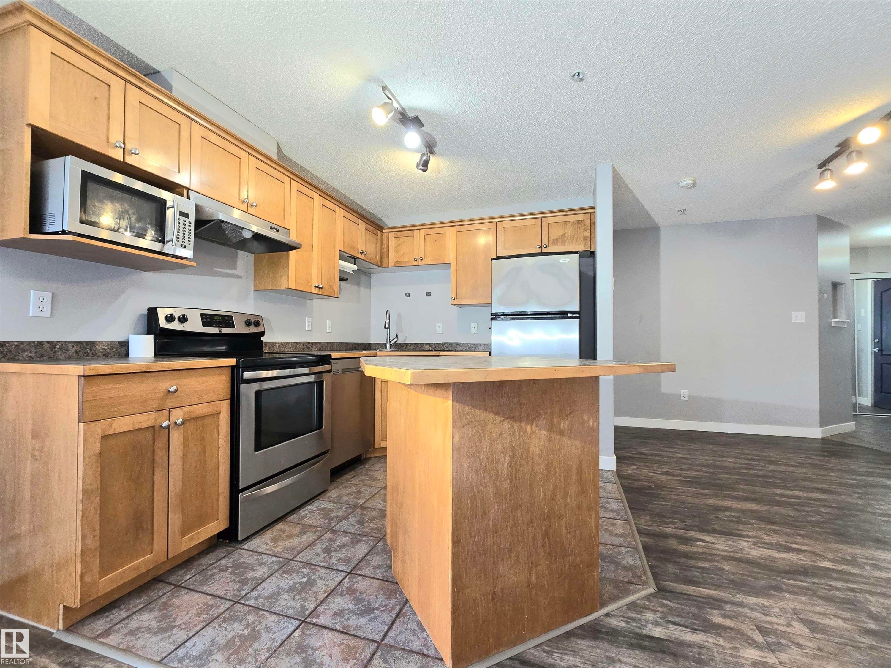 Kitchen featuring light wood cabinetry, stainless steel appliances, laminate countertop, and a peninsula with breakfast bar seating - #105 155 Edwards Dr Sw, Edmonton, AB - Indoor Photo Showing Kitchen