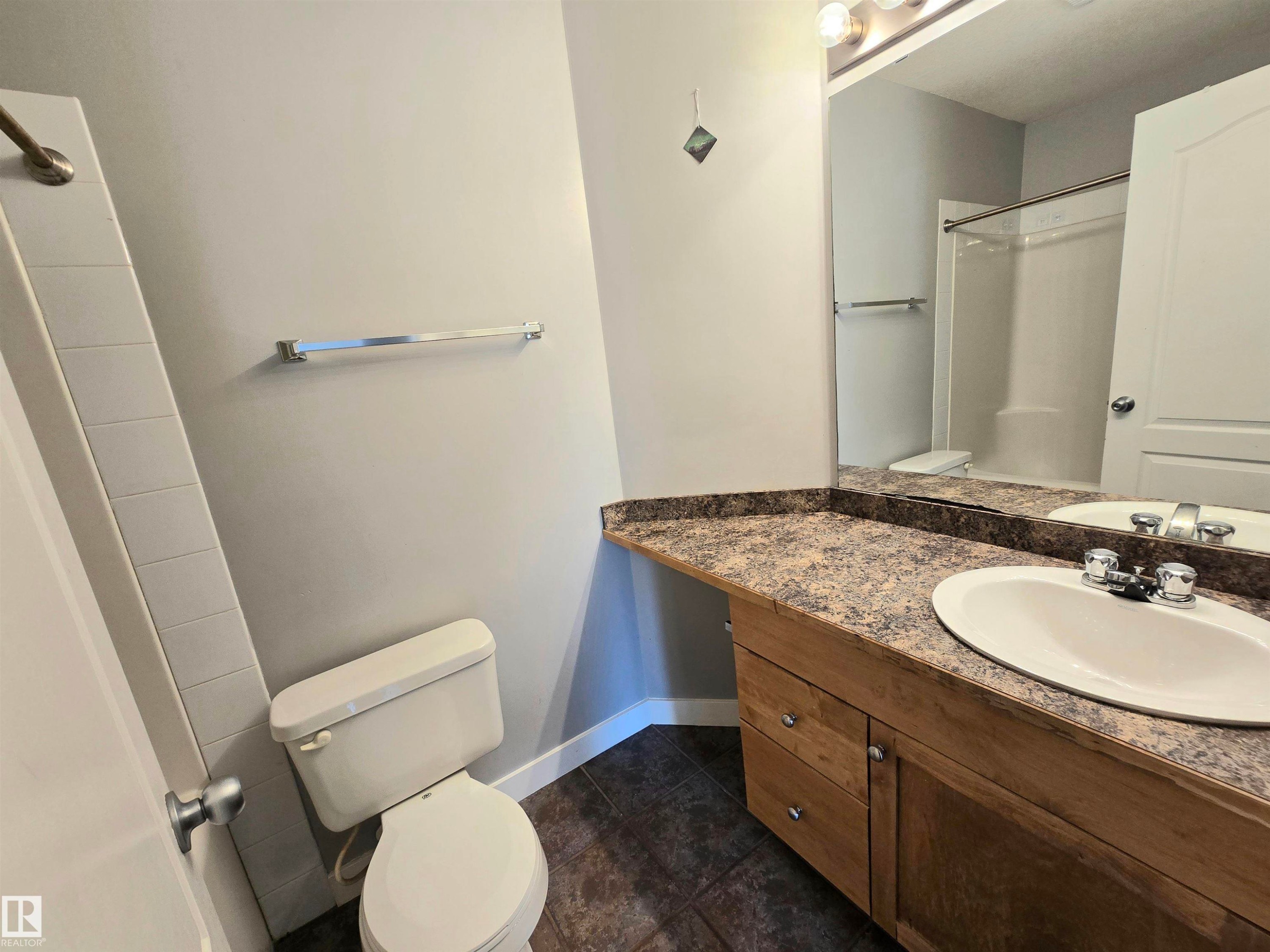Bathroom featuring a wood-finish vanity with a laminate countertop, an undermount sink, and a chrome faucet - #105 155 Edwards Dr Sw, Edmonton, AB - Indoor Photo Showing Bathroom