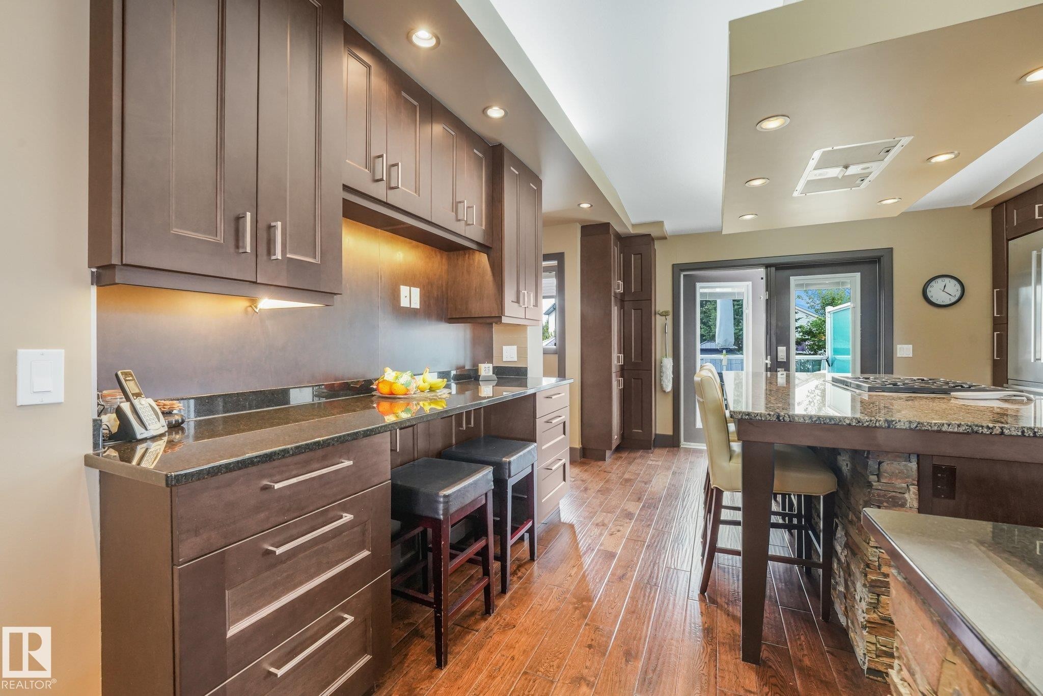 Rich wood-finish flooring, dark wood cabinetry, recessed lighting, stone-clad kitchen island, and glass-paned double doors - 12827 150 Avenue Nw, Edmonton, AB