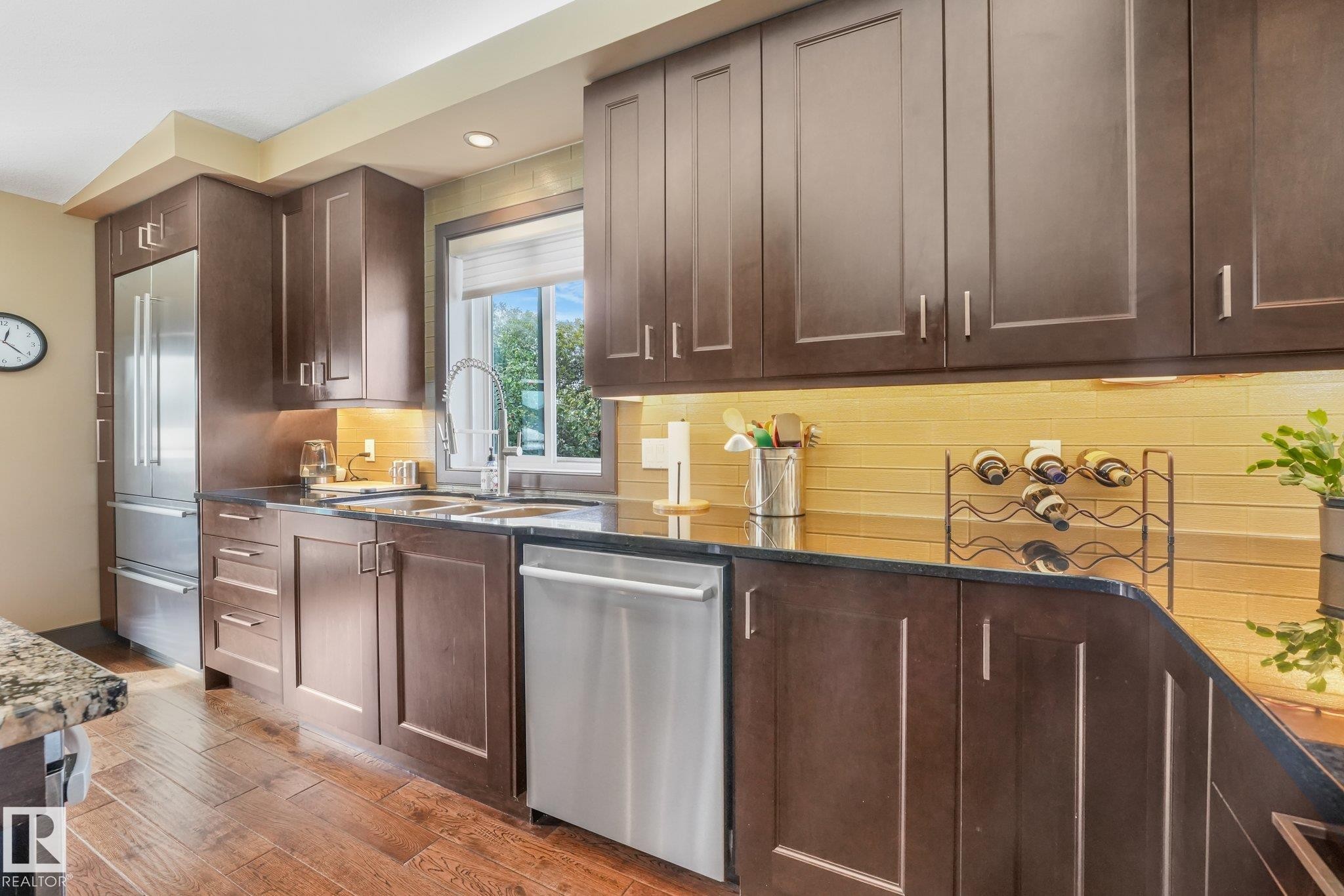 Hardwood-style flooring, dark wood-finish cabinetry, stainless steel appliances, dark countertops, and a tiled backsplash - 12827 150 Avenue Nw, Edmonton, AB