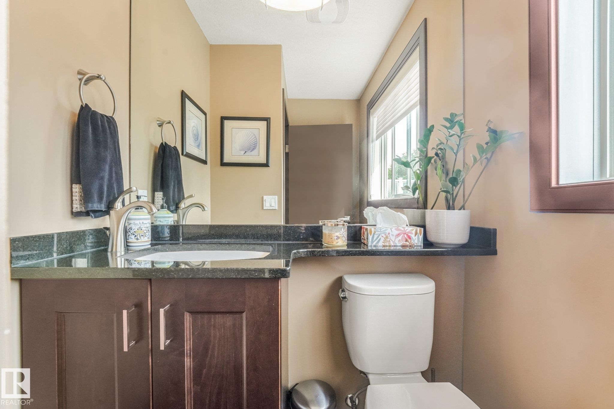 Wood-finish vanity with a drop-in sink, dark stone countertop, and brushed nickel faucet - 12827 150 Avenue Nw, Edmonton, AB