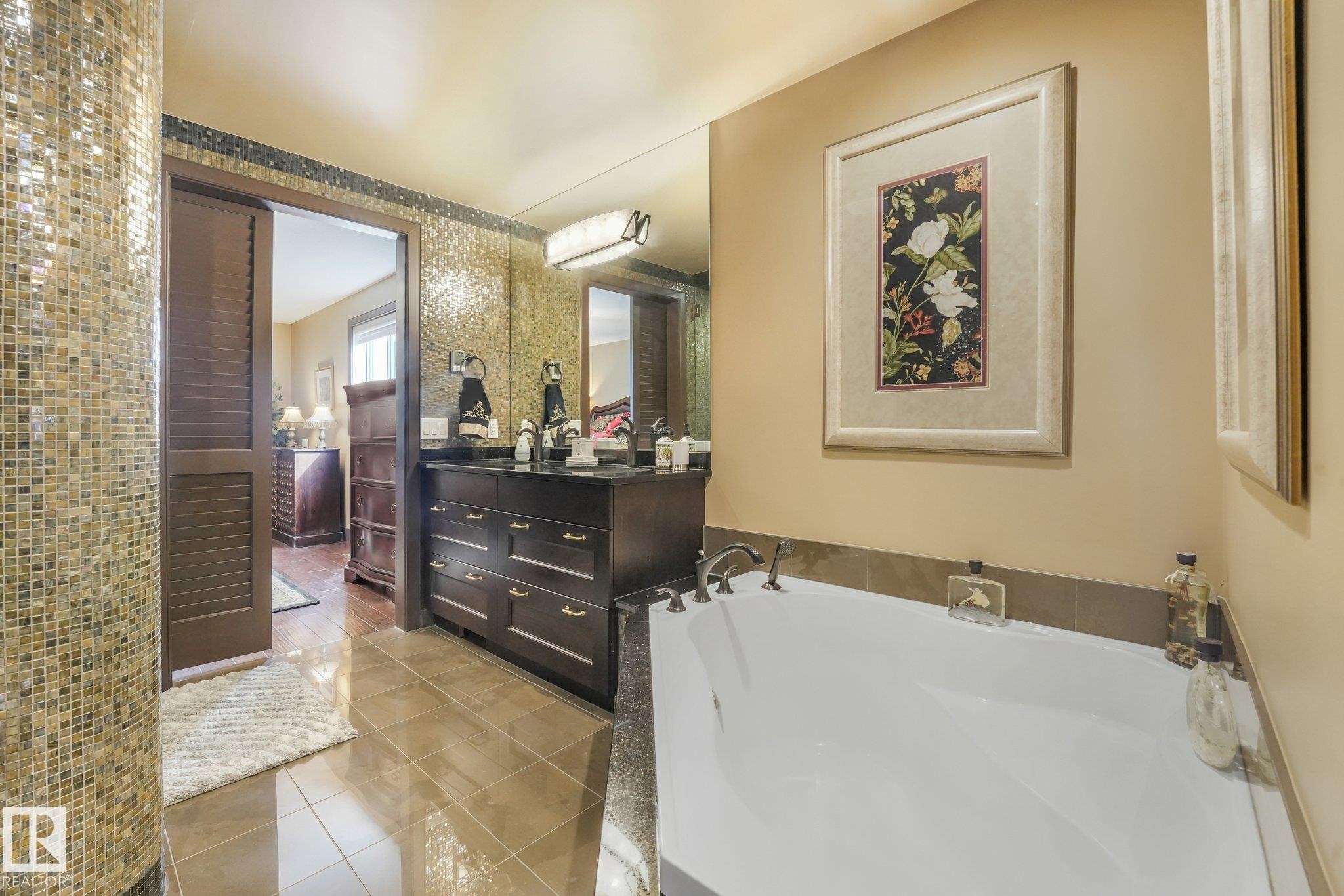 Bathroom featuring a built-in tub, dark wood-finish vanity with dual sinks, mosaic tile wall, and tiled flooring - 12827 150 Avenue Nw, Edmonton, AB