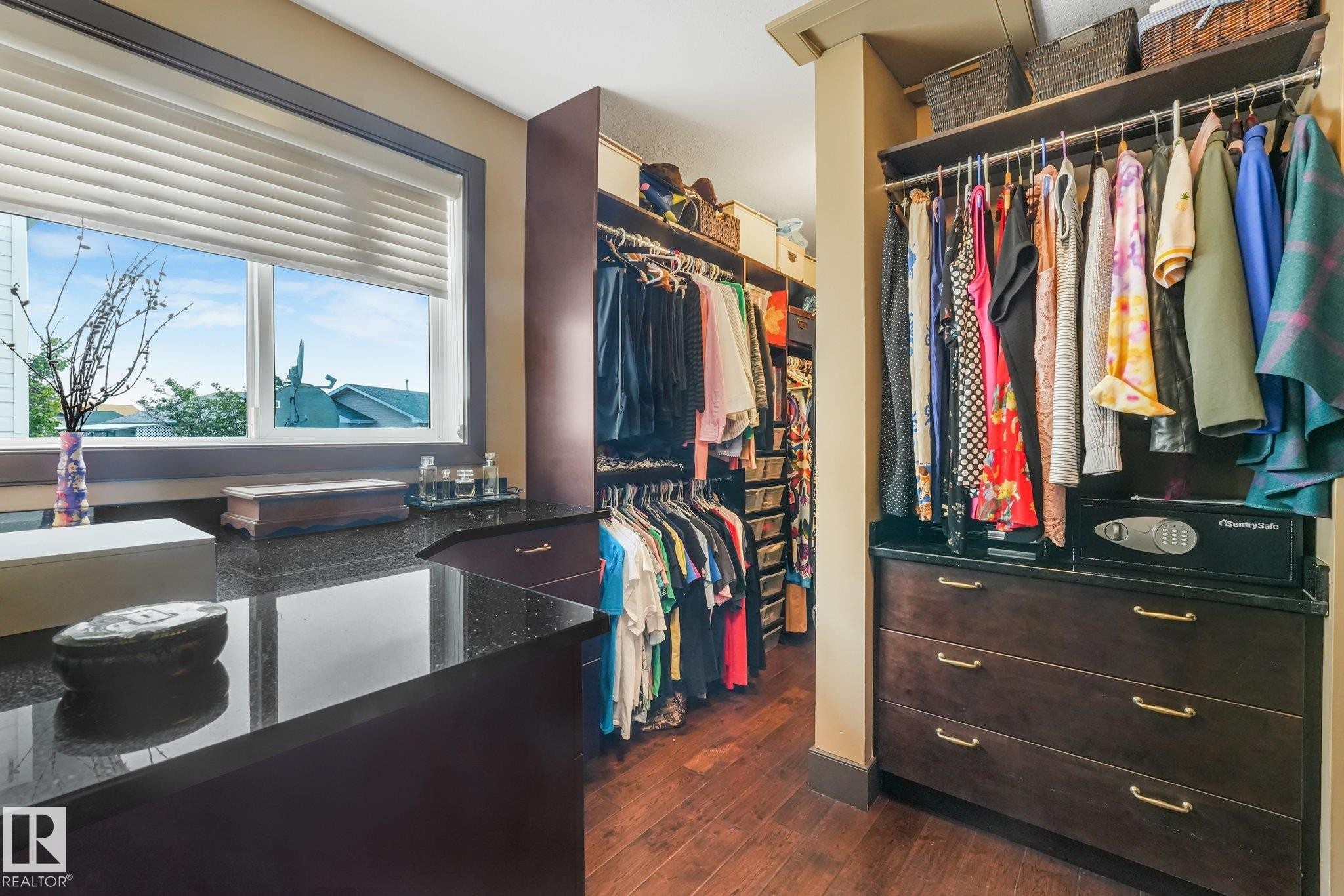 Custom closet system featuring built-in cabinetry, polished dark countertops, ample hanging storage, and rich wood-finish flooring - 12827 150 Avenue Nw, Edmonton, AB