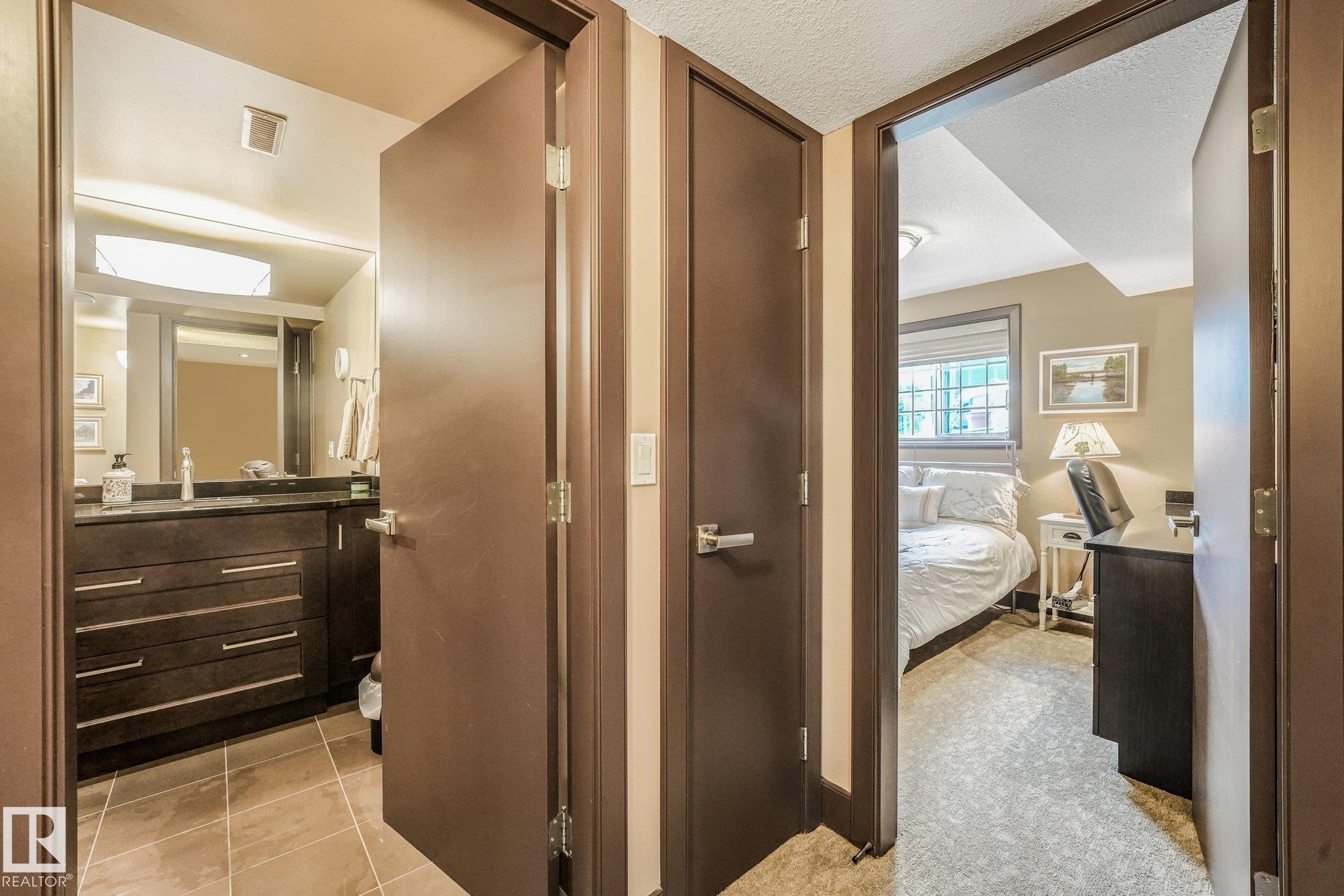 Dark wood-finish doors with brushed nickel hardware, bathroom featuring a dark wood-finish vanity with drawer storage and a dark countertop, tile flooring, and a framed mirror - 12827 150 Avenue Nw, Edmonton, AB