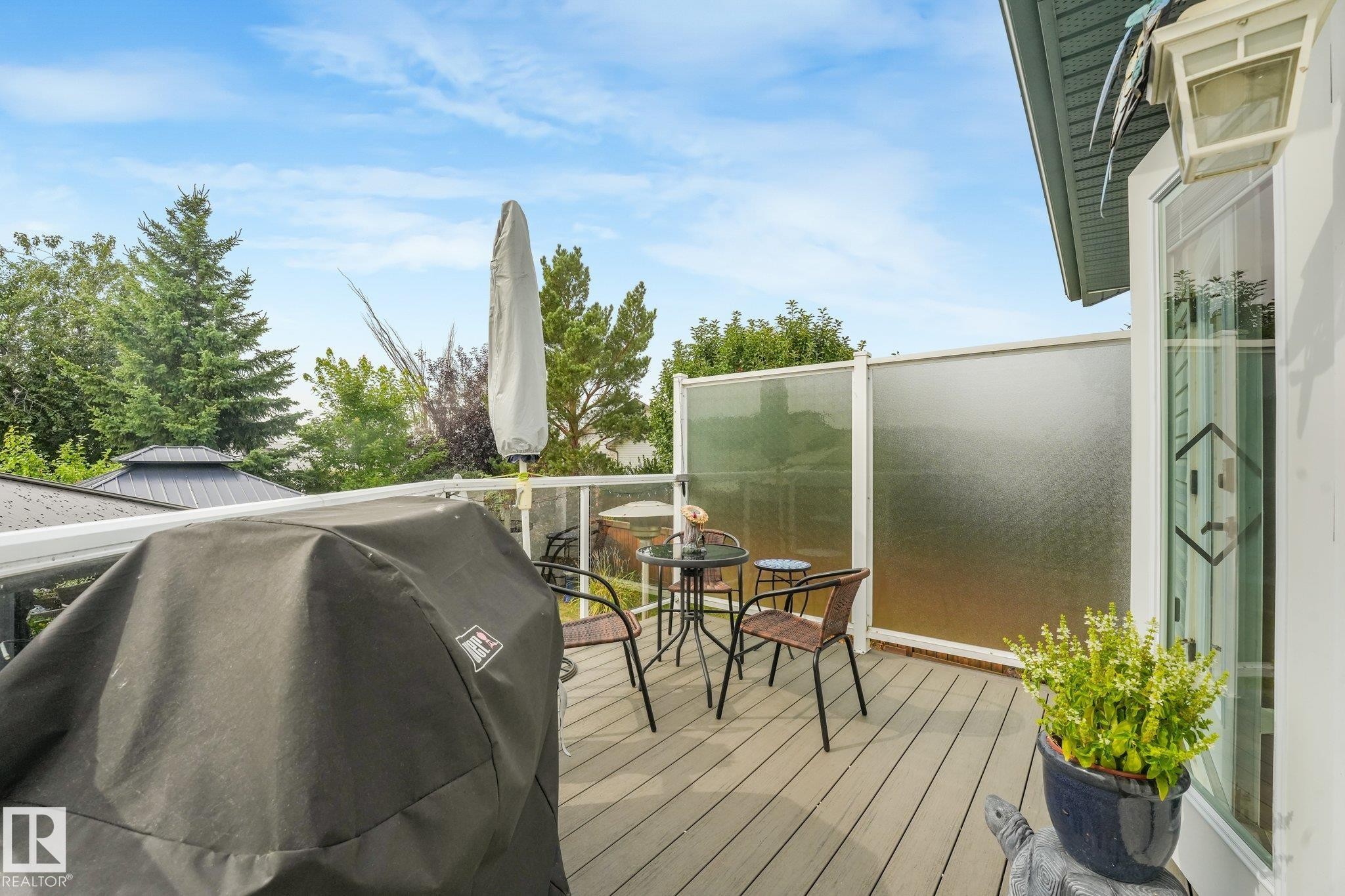 Deck featuring composite wood-finish flooring, glass panel railing, and privacy screen - 12827 150 Avenue Nw, Edmonton, AB