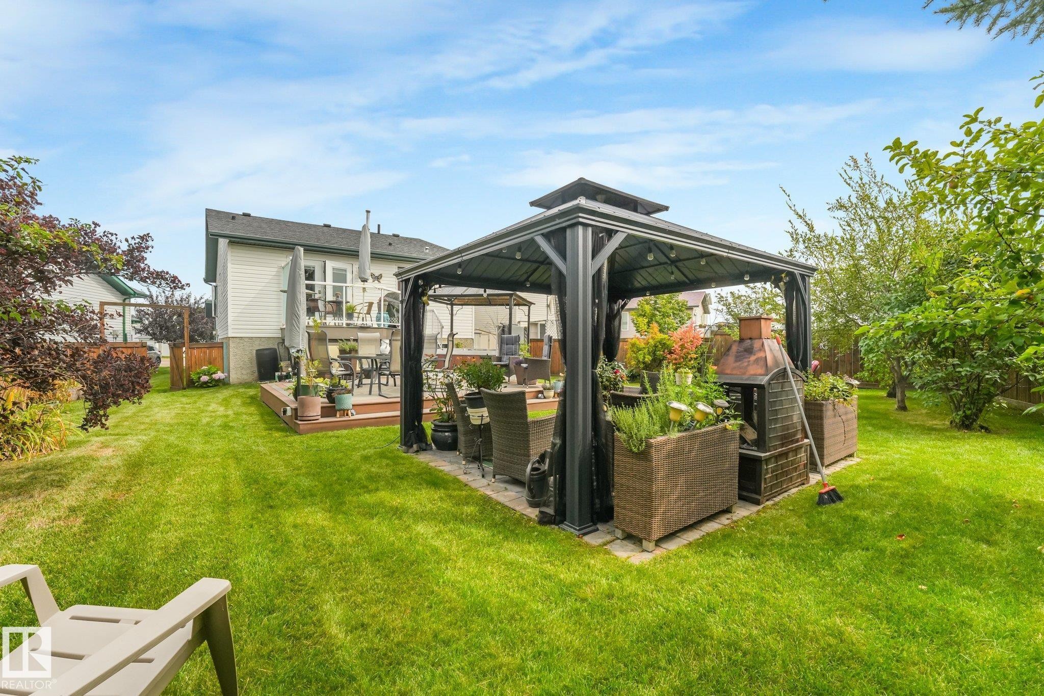Expansive grassy yard with a multi-level wood deck, a covered patio area with pavers, a built-in outdoor cooking feature, and established landscaping - 12827 150 Avenue Nw, Edmonton, AB