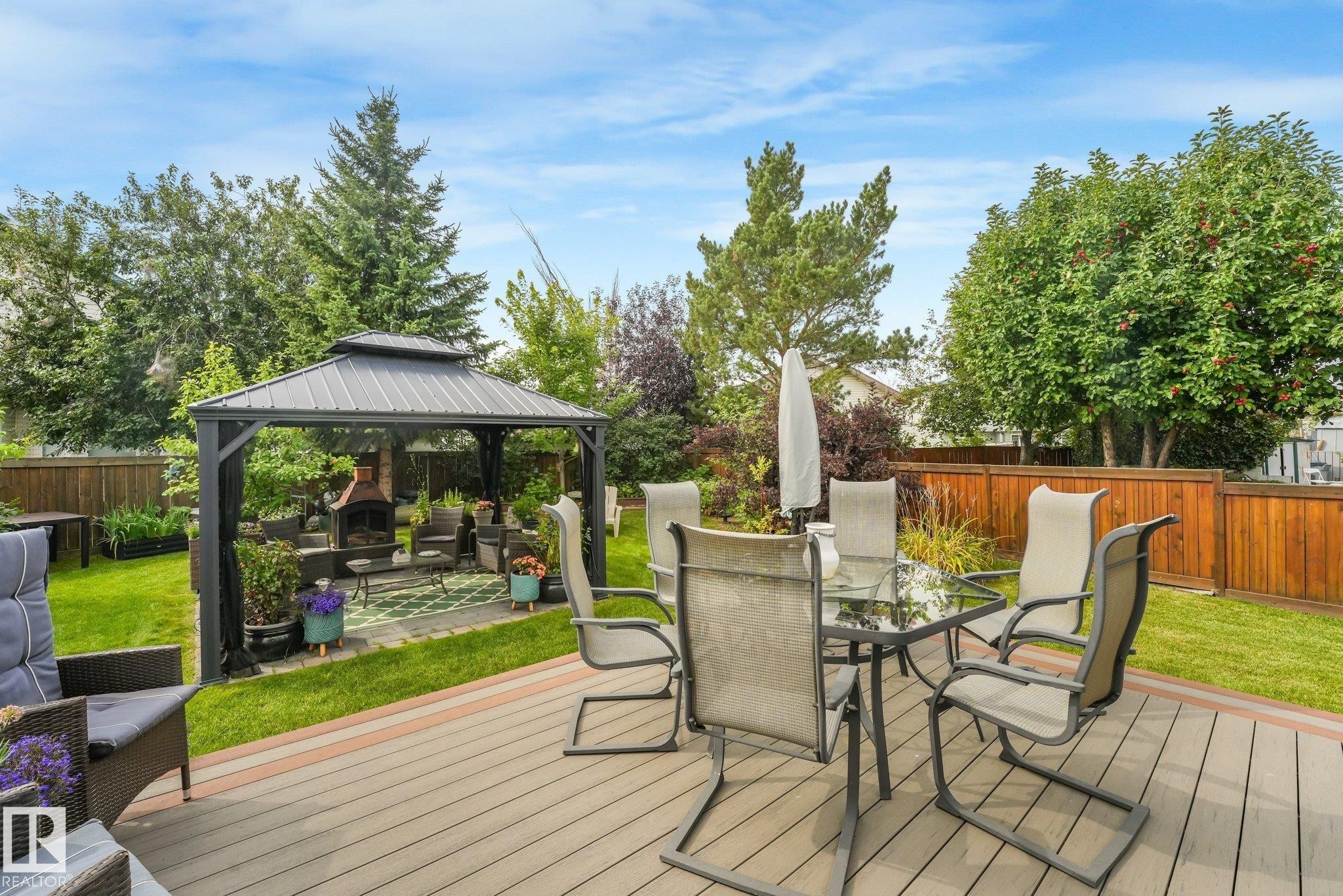 Expansive backyard featuring a composite deck, a metal-roof gazebo, a brick fireplace, and mature trees - 12827 150 Avenue Nw, Edmonton, AB